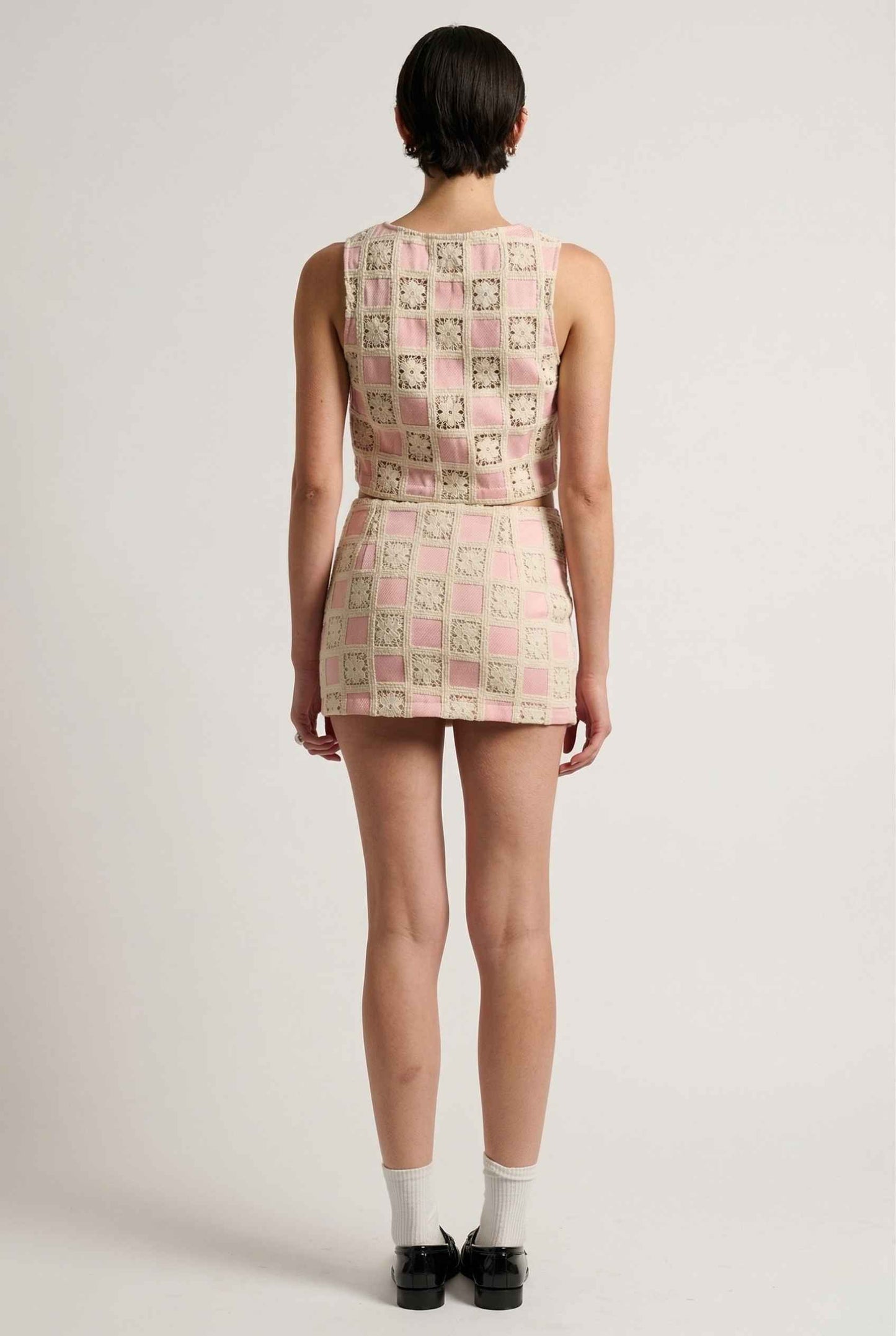 Model wearing Daphne Skirt in Pink Modern Jacquard Checkerboard Mini Skirt with matching vest top and shiny loafers with tall socks