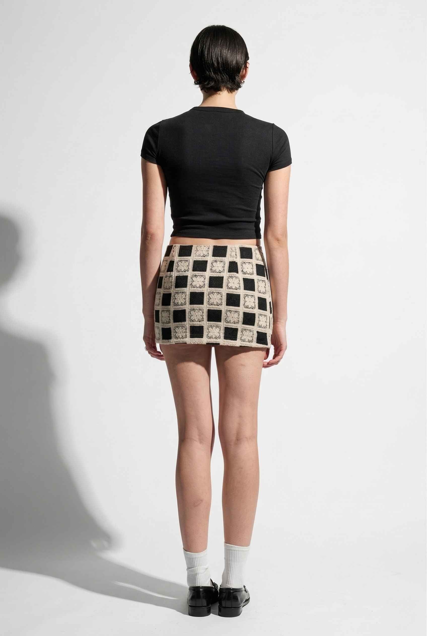 Model wearing Daphne Skirt in Black Modern Jacquard Checkerboard Mini Skirt with basic top and shiny loafers with tall socks
