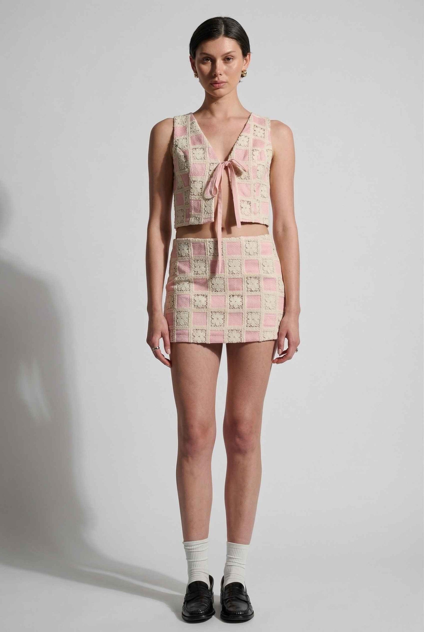 Model wearing Daphne Skirt in Pink Modern Jacquard Checkerboard Mini Skirt with matching vest top and shiny loafers with tall socks