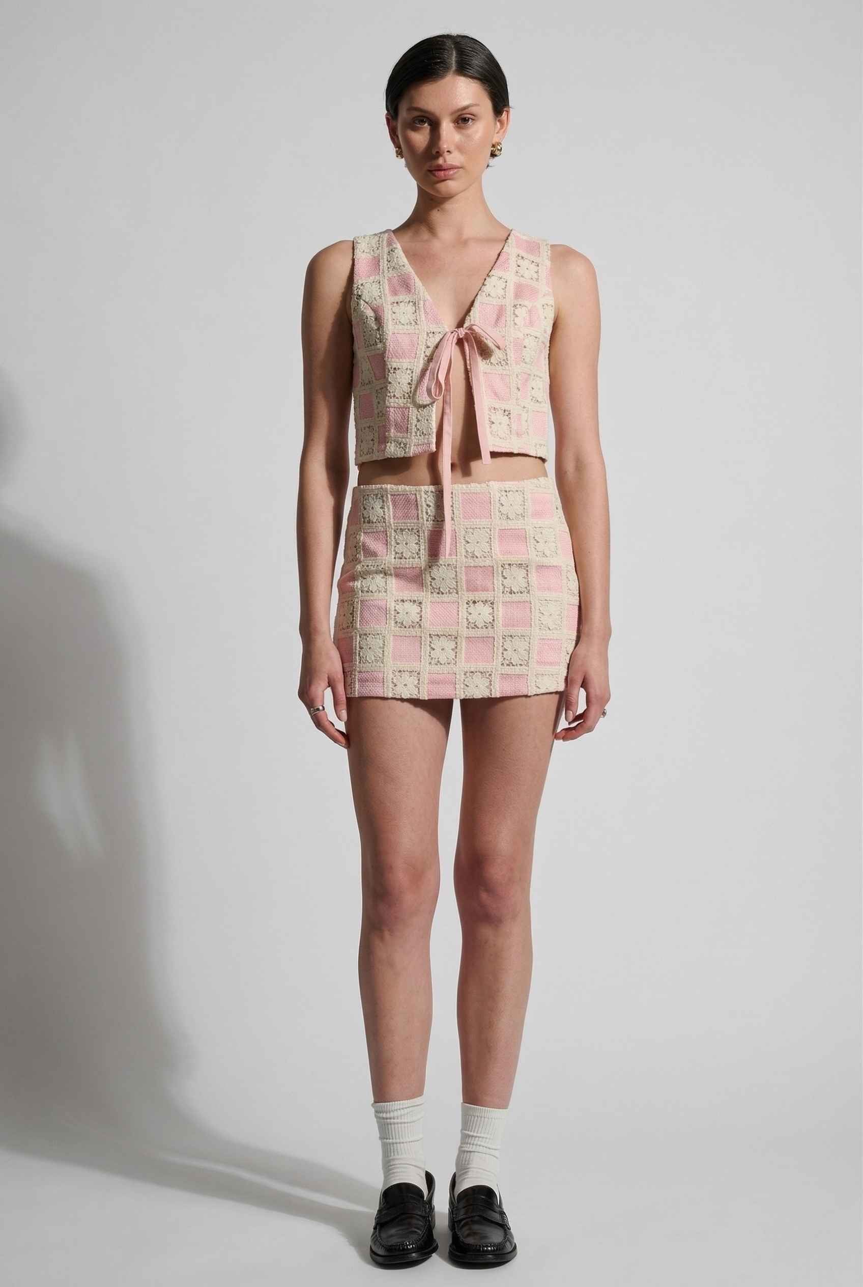Model wearing Daphne Skirt in Pink Modern Jacquard Checkerboard Mini Skirt with matching vest top and shiny loafers with tall socks