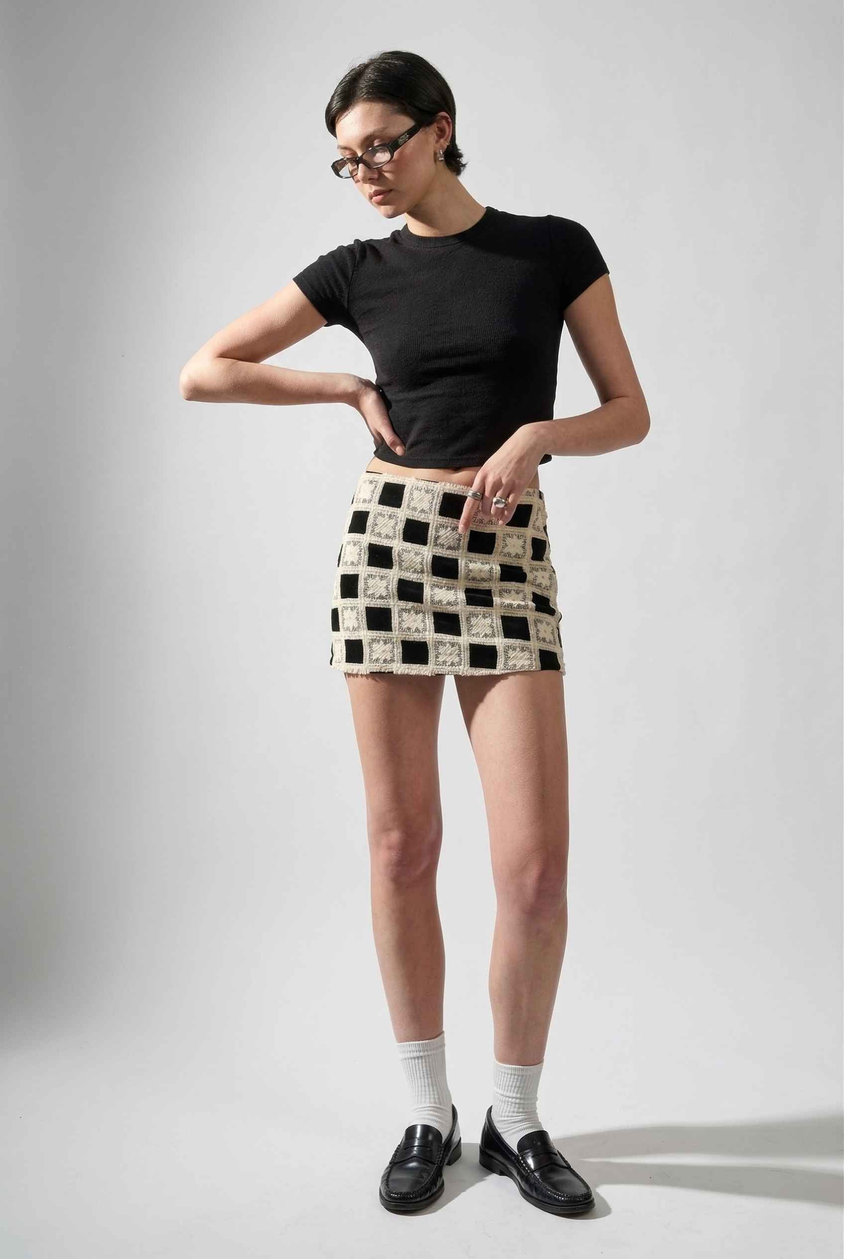 Model wearing Daphne Skirt in Black Modern Jacquard Checkerboard Mini Skirt with basic top and shiny loafers with tall socks