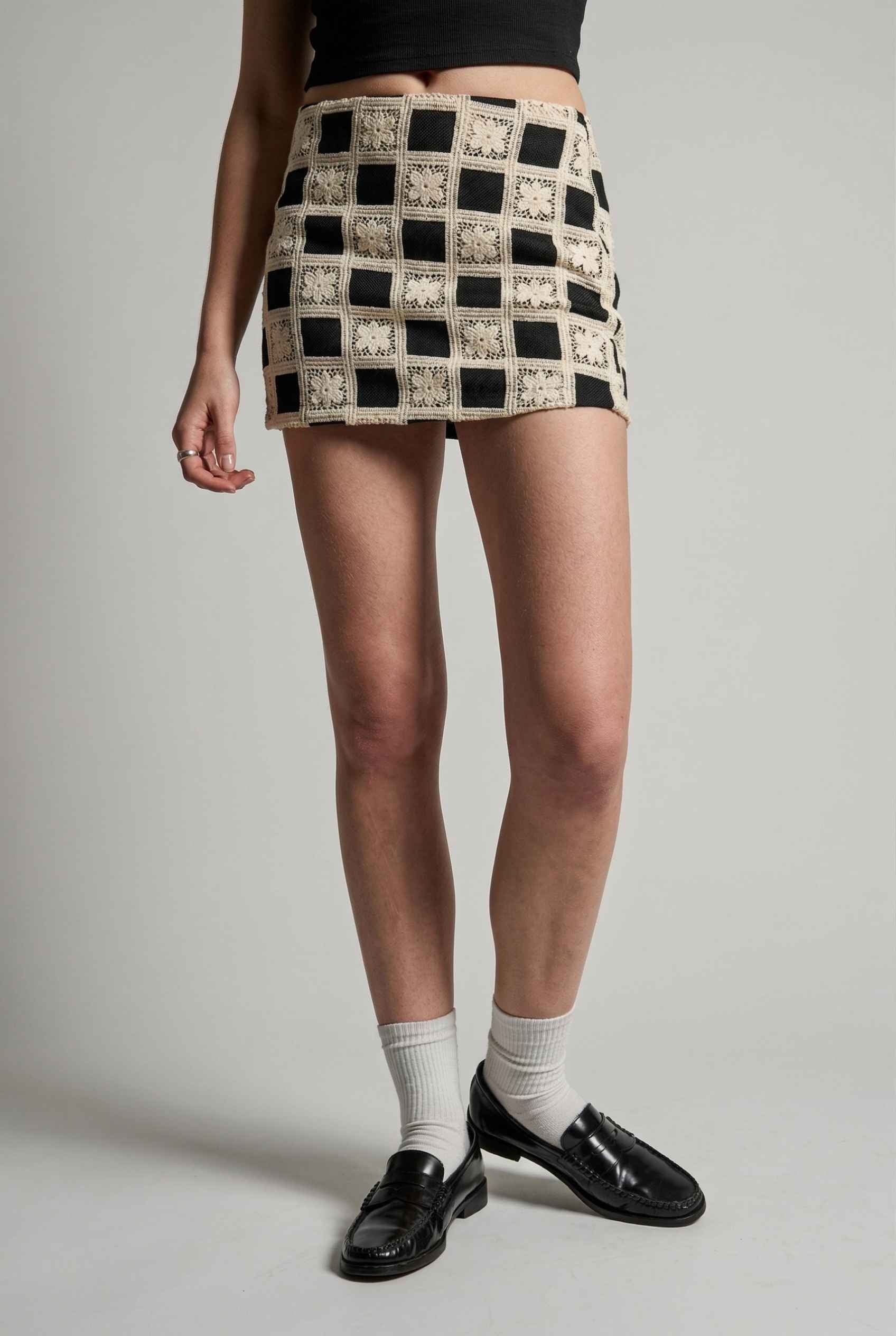 Model wearing Daphne Skirt in Black Modern Jacquard Checkerboard Mini Skirt with basic top and shiny loafers with tall socks