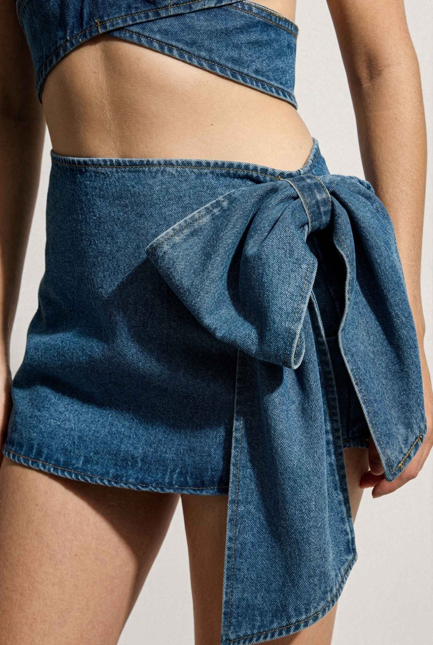Model wearing Darcy Skirt in Medium Wash Cotton Denim Mini Skirt with Bow paired with matching bra top close up bow detail