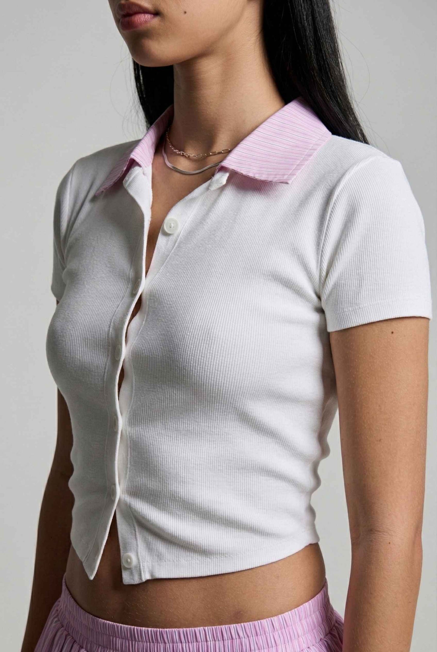 Woman wearing a Darcy Top White & Pink Contrast Collar Button Down Knit with a pink collar against a gray background