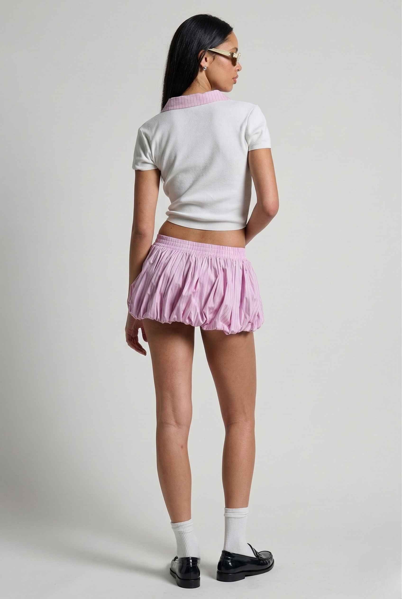 Woman wearing a Darcy Top White & Pink Contrast Collar Button Down Knit and pink skirt on a plain background