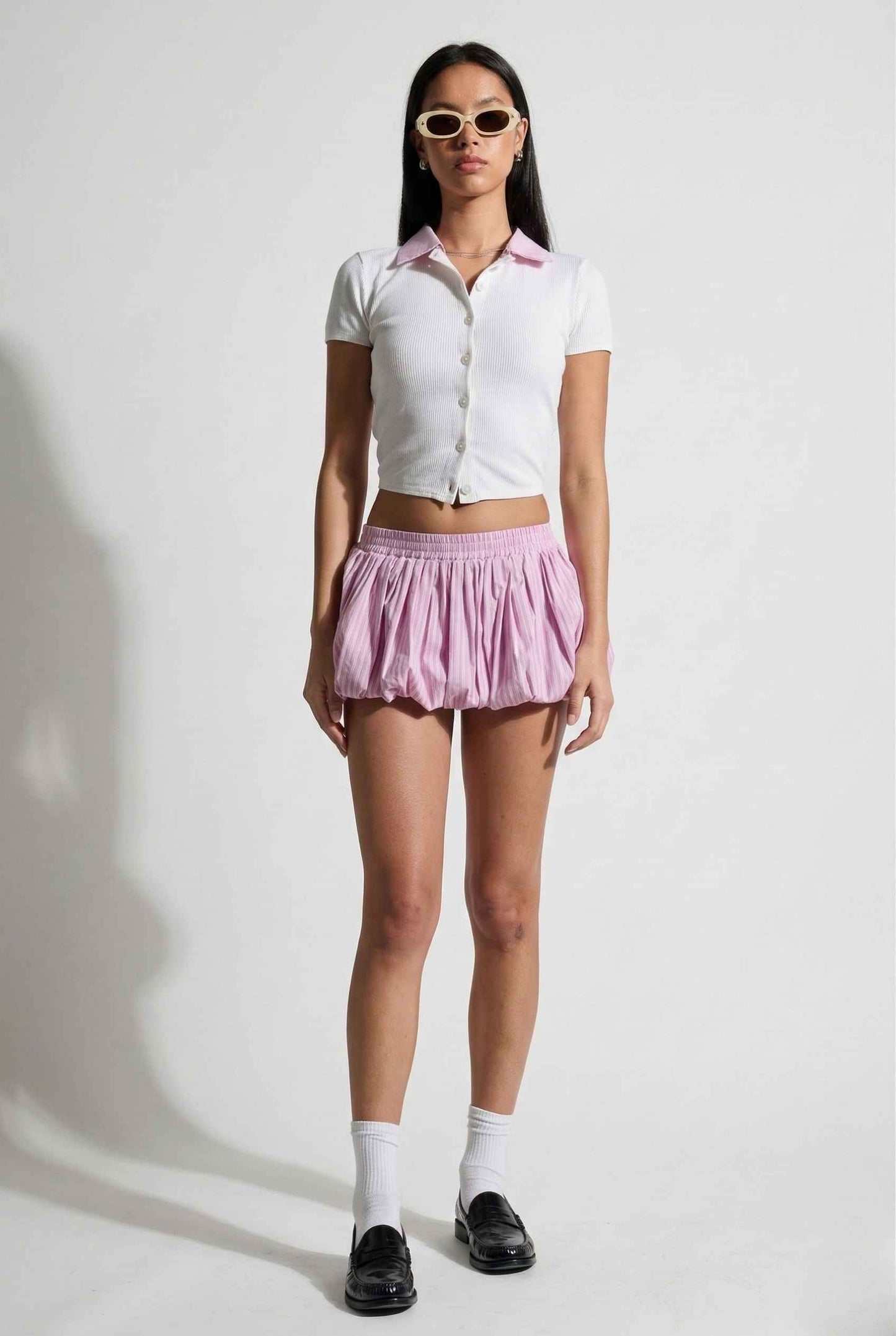 Woman wearing a Darcy Top White & Pink Contrast Collar Button Down Knit and pink skirt with sunglasses on a white background