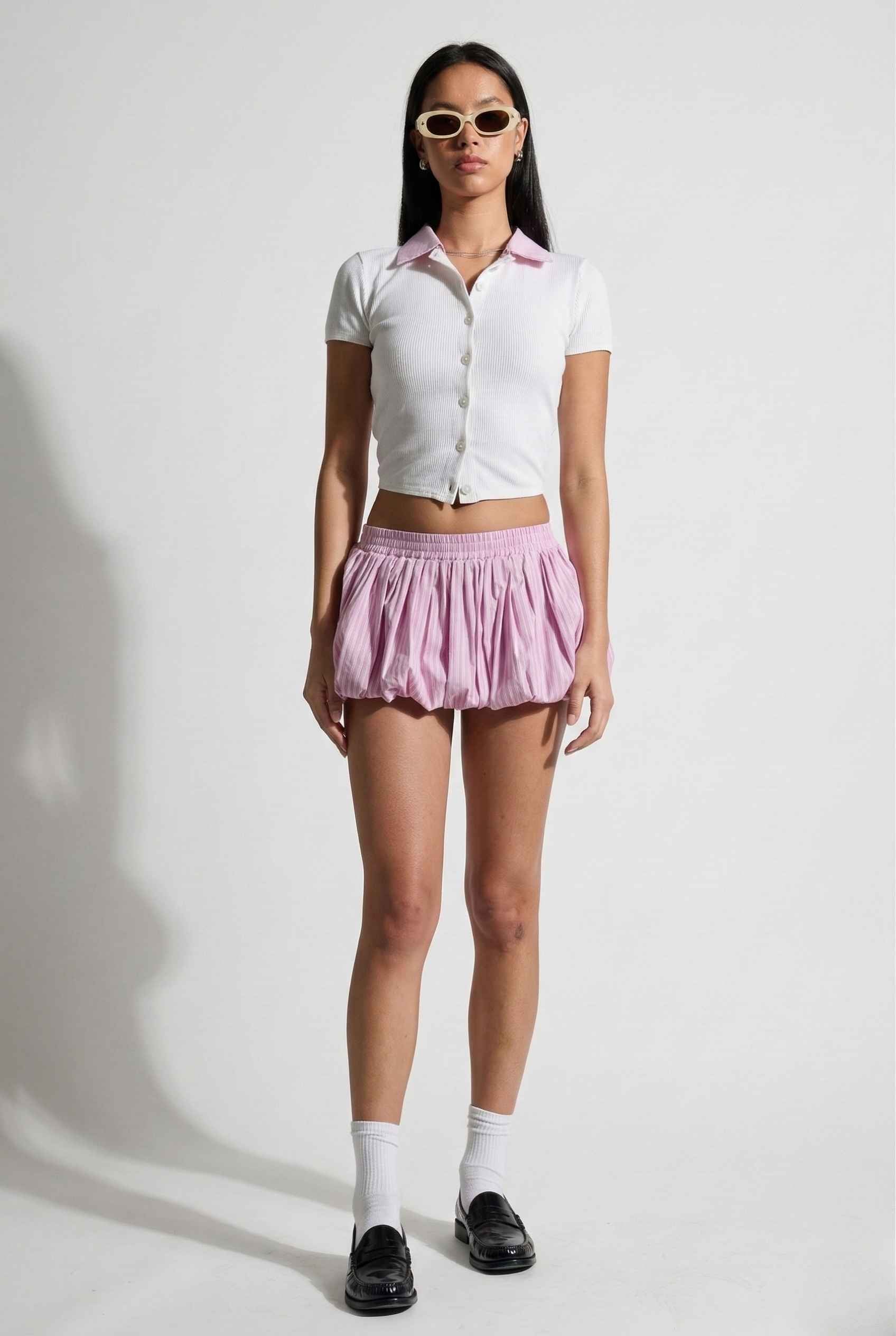 Woman wearing a Darcy Top White & Pink Contrast Collar Button Down Knit and pink skirt with sunglasses on a white background