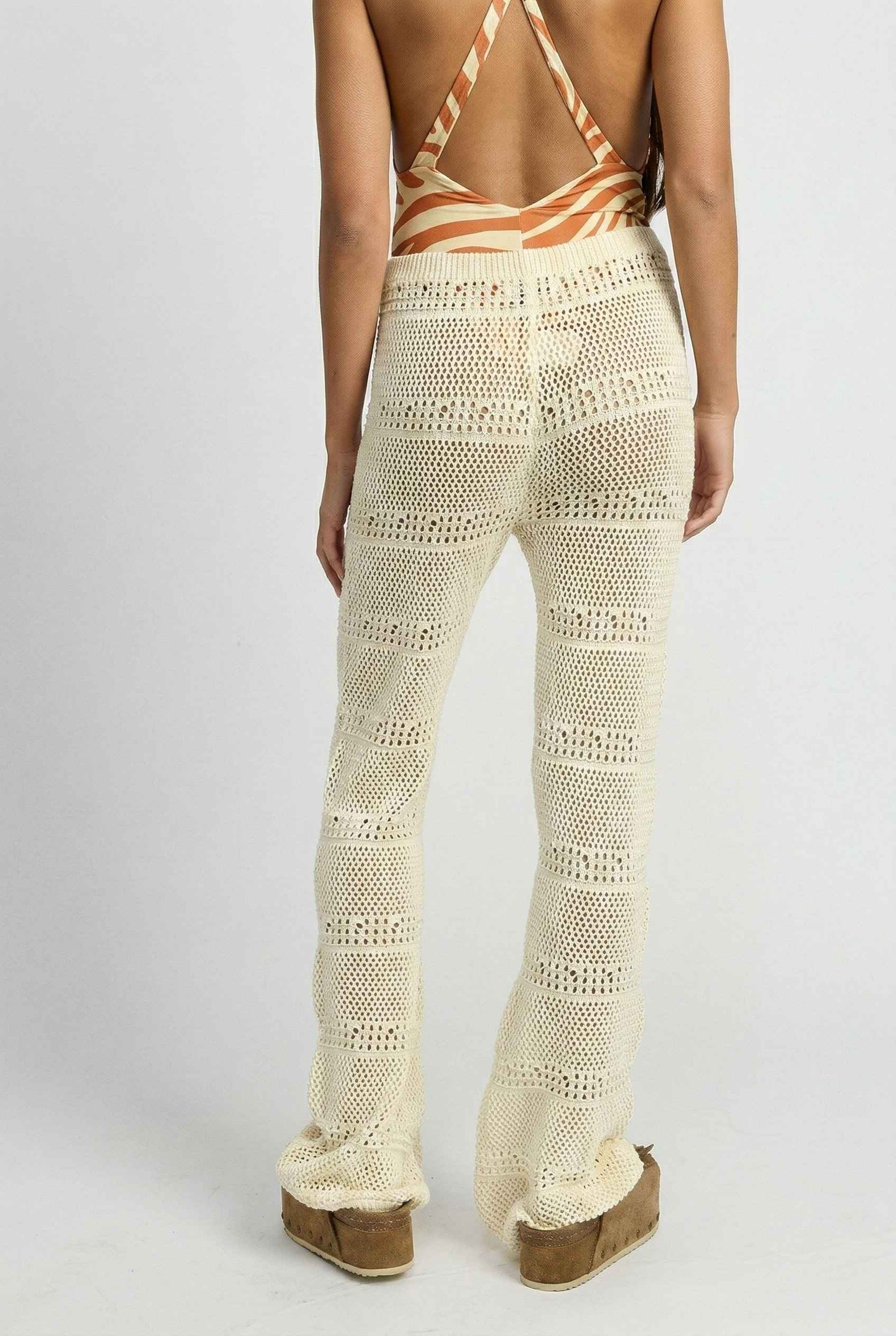 Model wearing Eden Pants in Cream Cotton Crochet Drawstring Beach Trousers with swimsuit and platform sandals on a plain background