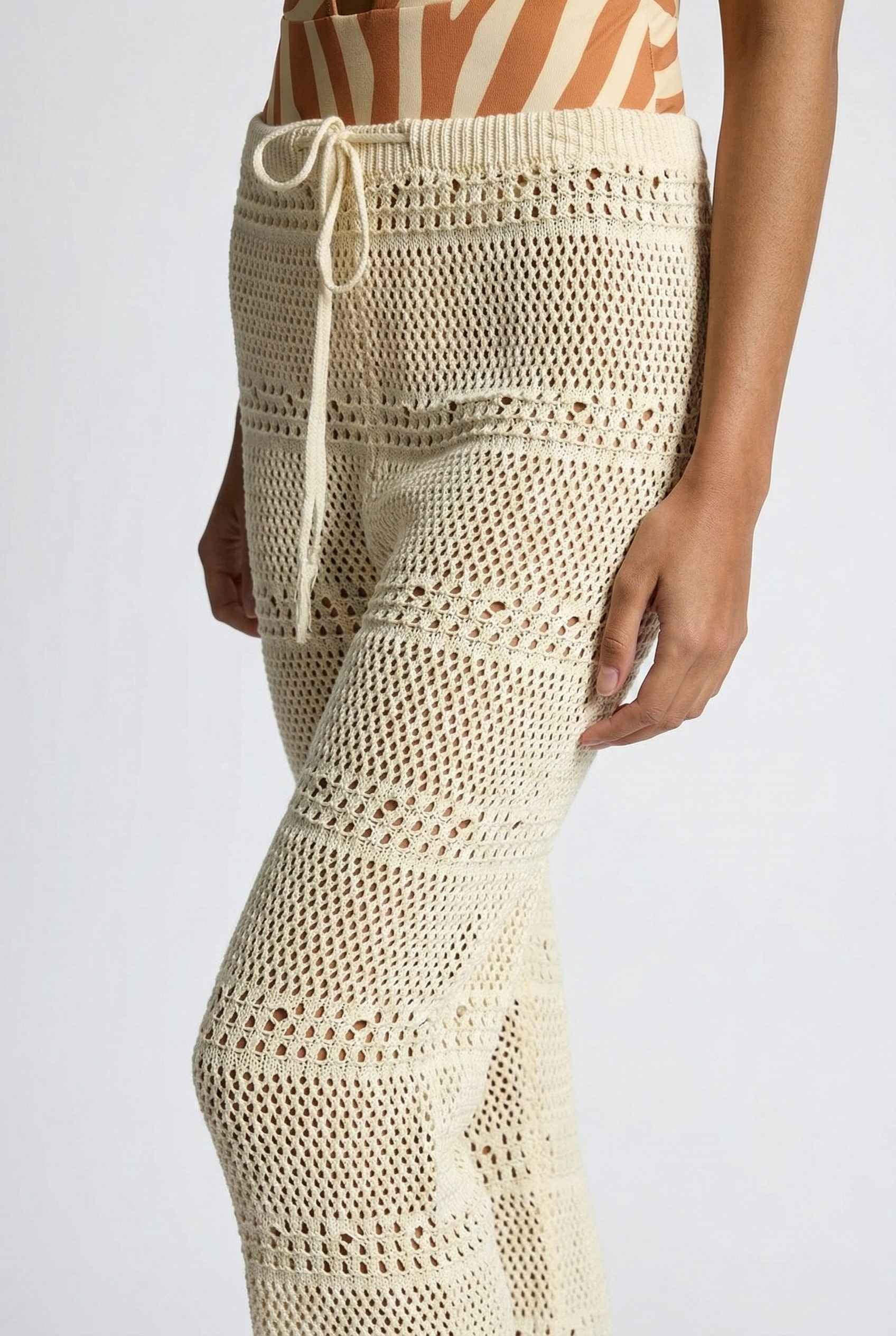 Model wearing Eden Pants in Cream Cotton Crochet Drawstring Beach Trousers with swimsuit on a plain background
