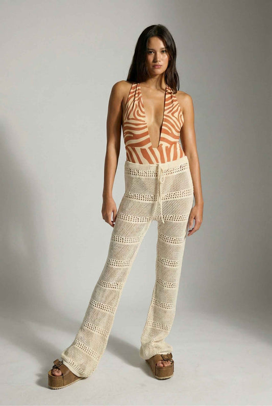 Model wearing Eden Pants in Cream Cotton Crochet Drawstring Beach Trousers with swimsuit and platform sandals on a plain background