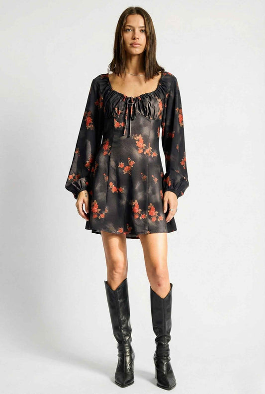 Woman wearing a Elara Mini Black Rose Print Long Sleeve Dress  with long sleeves and black knee-high boots on a white background