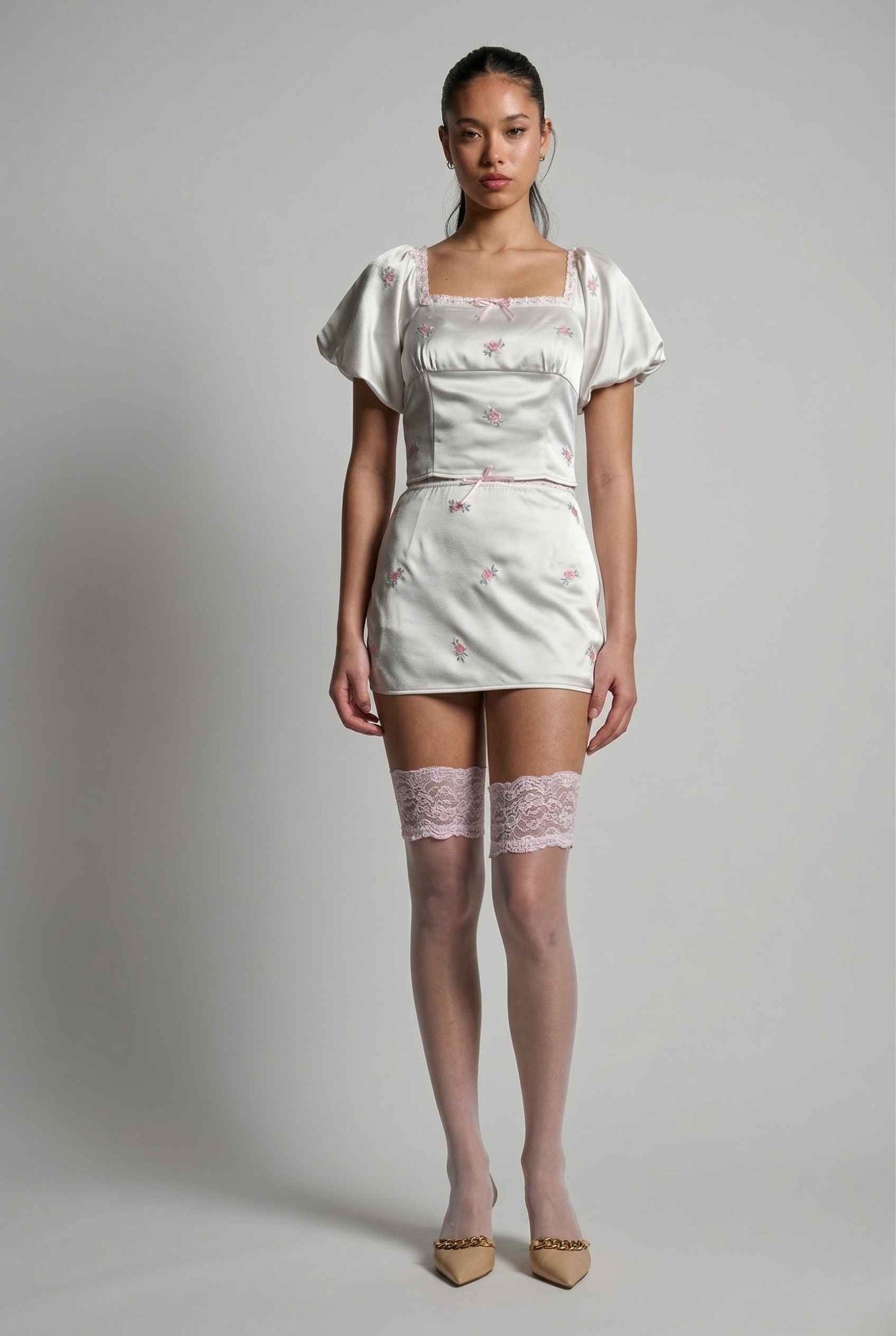 Model wearing a Elara Skirt White Satin Mini Skirt with Dainty Pink Florals with lace details on a plain background