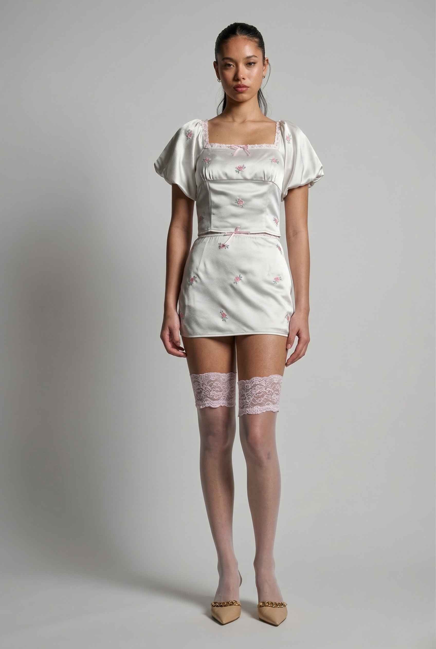 Model wearing a Elara Skirt White Satin Mini Skirt with Dainty Pink Florals with lace details on a plain background