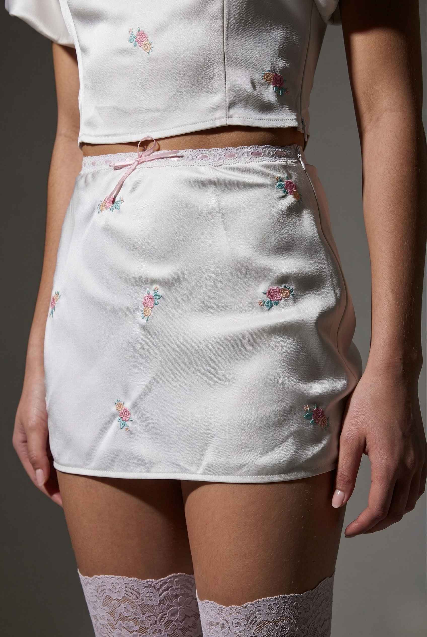 Elara Skirt White Satin Mini Skirt with Dainty Pink Florals with floral embroidery worn by a person on a gray background