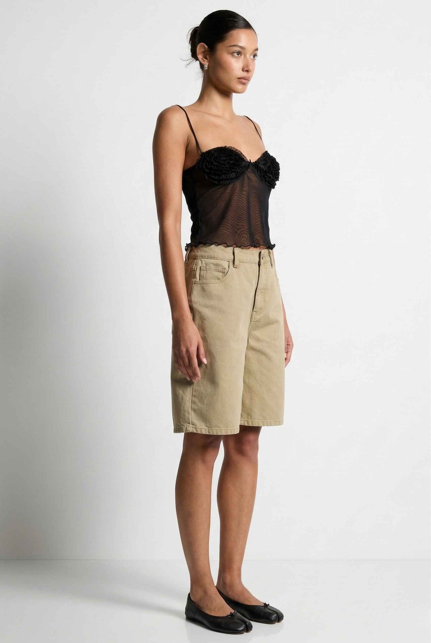 Woman wearing a Elara Top Black Sheer Mesh Camisole with 3D Floral Cups with sheer overlay and beige skirt on a background