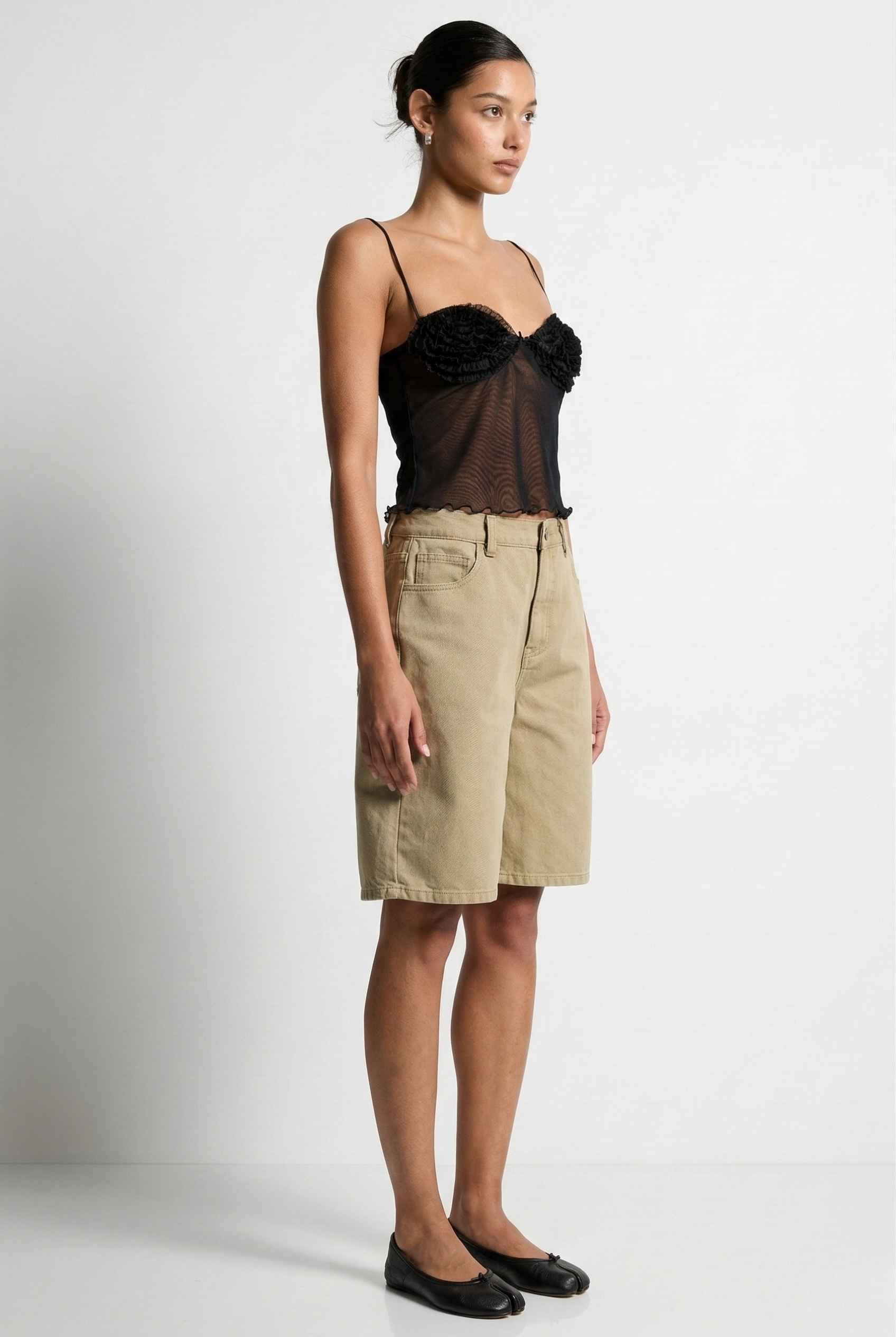 Woman wearing a Elara Top Black Sheer Mesh Camisole with 3D Floral Cups with sheer overlay and beige skirt on a background