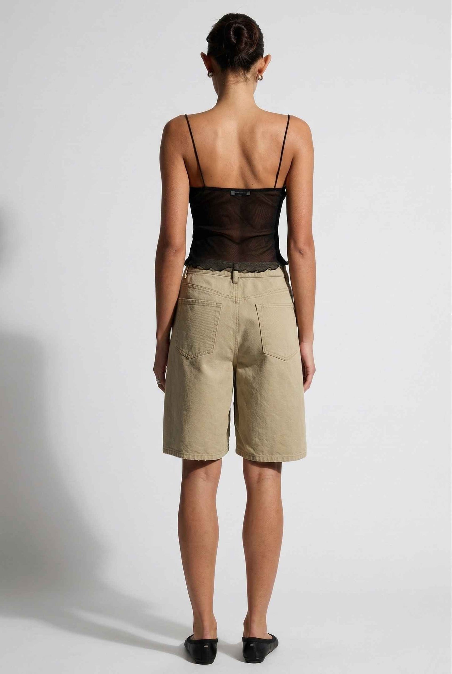 Woman wearing a Elara Top Black Sheer Mesh Camisole with 3D Floral Cups and beige shorts on a background