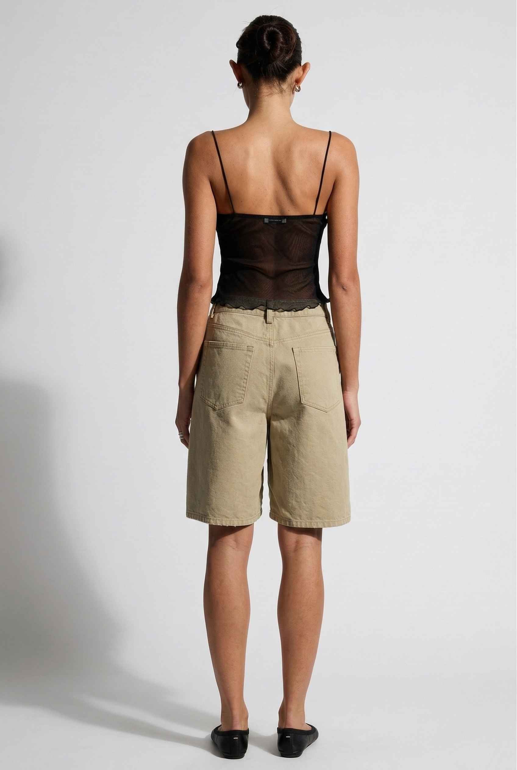 Woman wearing a Elara Top Black Sheer Mesh Camisole with 3D Floral Cups and beige shorts on a background