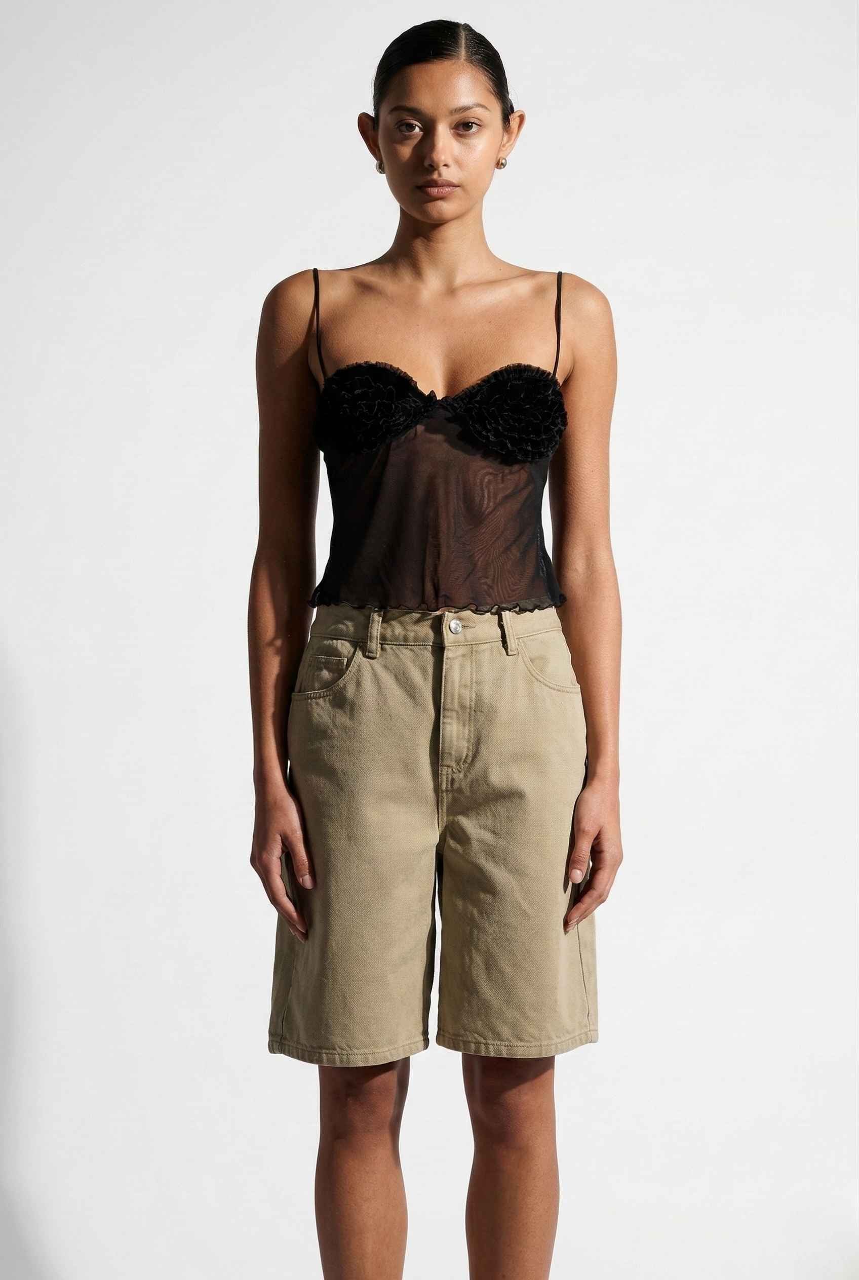 Woman wearing a Elara Top Black Sheer Mesh Camisole with 3D Floral Cups and beige shorts on a background