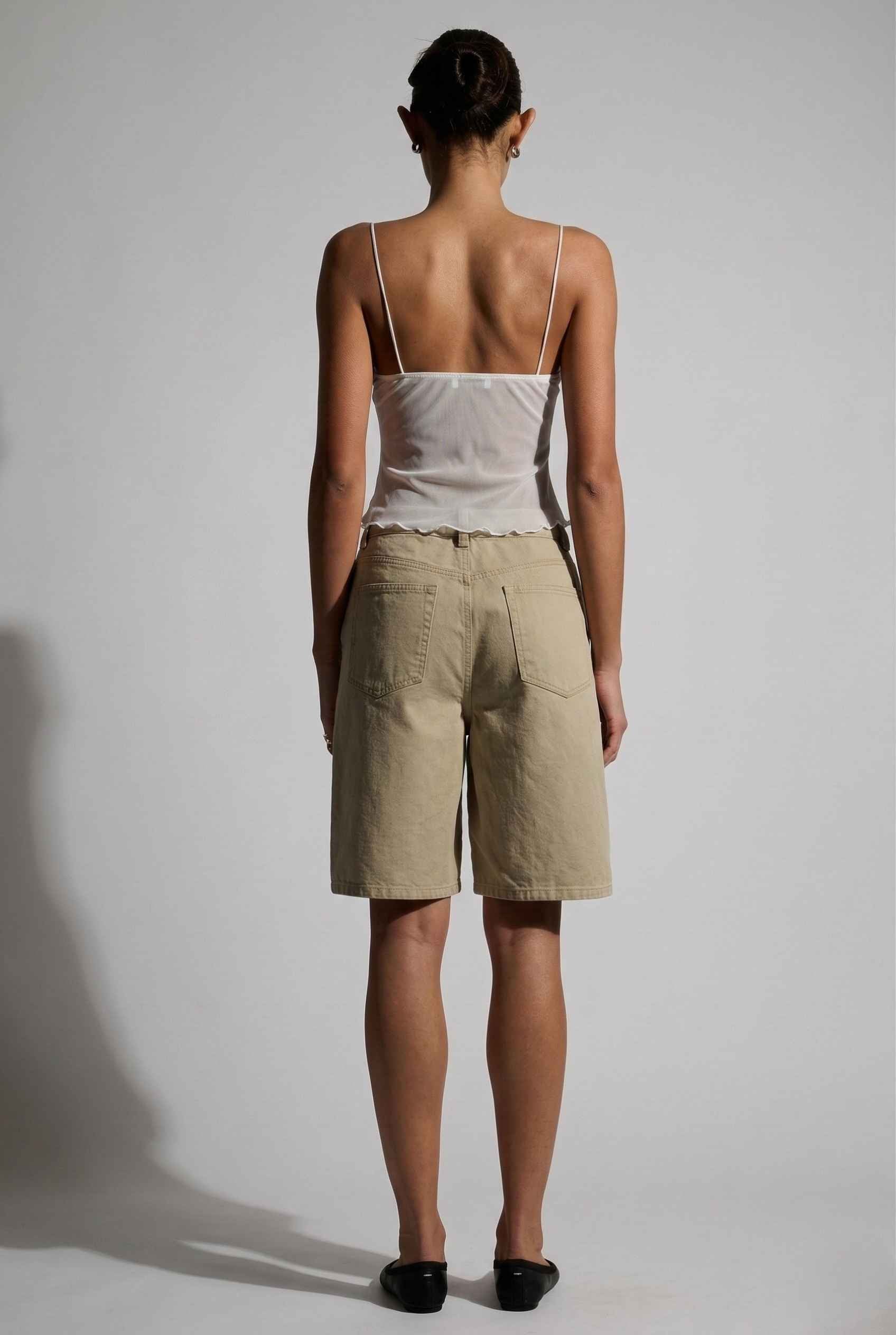 Woman wearing a Elara Top White Sheer Mesh Camisole with 3D Floral Cups and beige shorts against a plain background