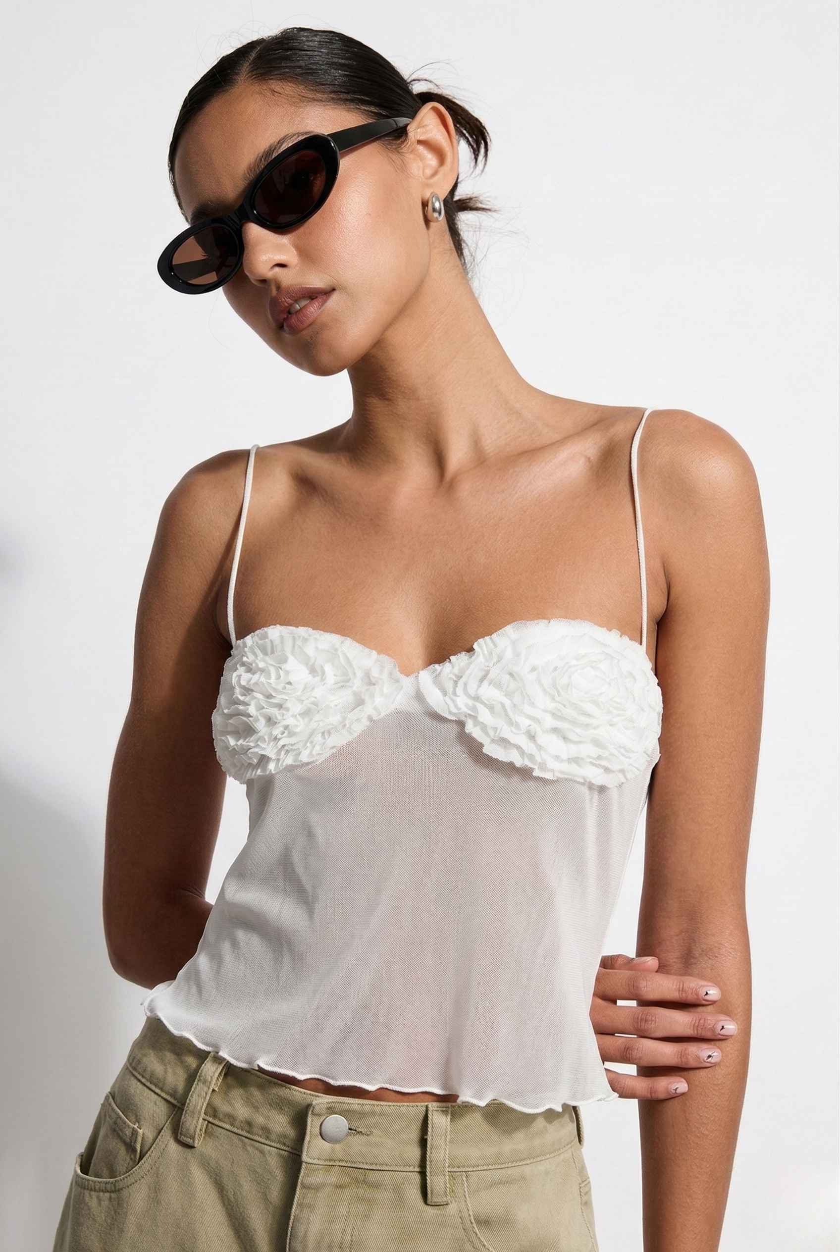 Woman wearing a Elara Top White Sheer Mesh Camisole with 3D Floral Cups and sunglasses on a plain background