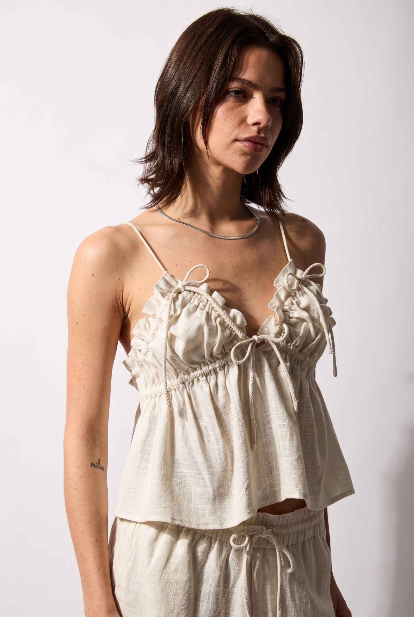 Model wearing Elena Ruffled Camisole Rayon-Linen Tank Top in Off White paired with matching smocked shorts close up bow details
