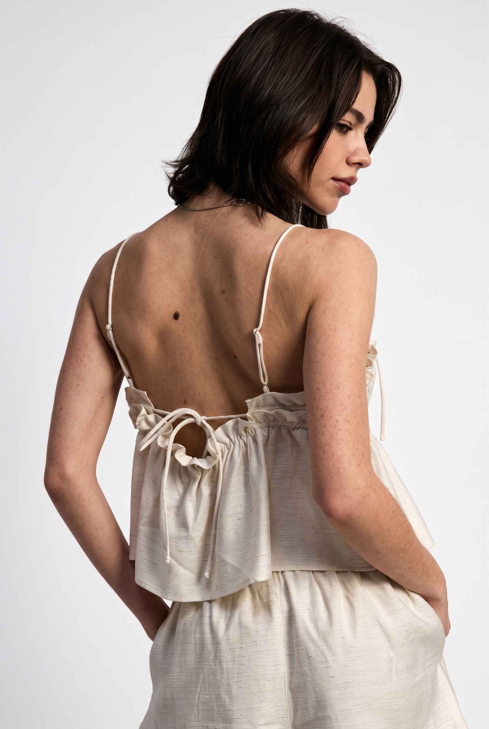 Model wearing Elena Ruffled Camisole Rayon-Linen Tank Top in Off White paired with matching smocked shorts back view