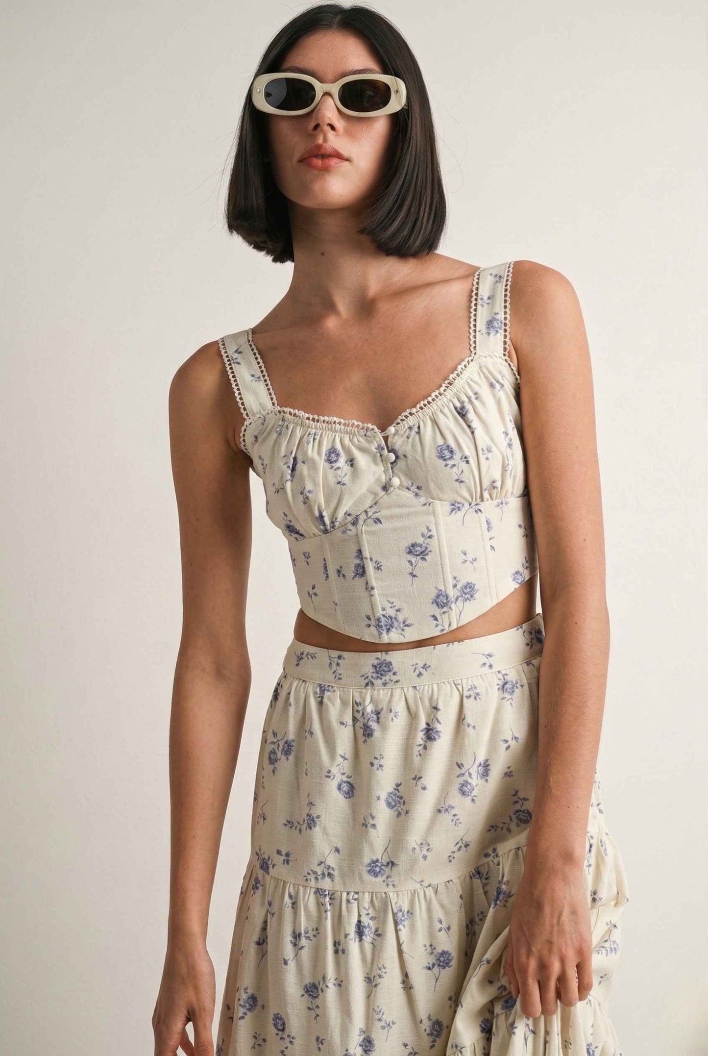 Woman wearing a Eliana Top White & Blue Floral Cotton Corset Crop and sunglasses against a plain background
