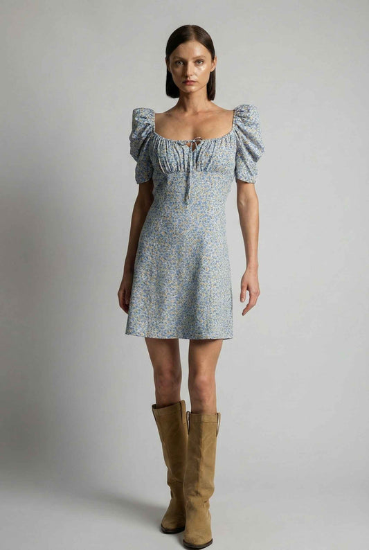 Woman wearing a Elise Mini Light Blue Puff Sleeve Floral Ruched Dress with puff sleeves and brown boots on a gray background