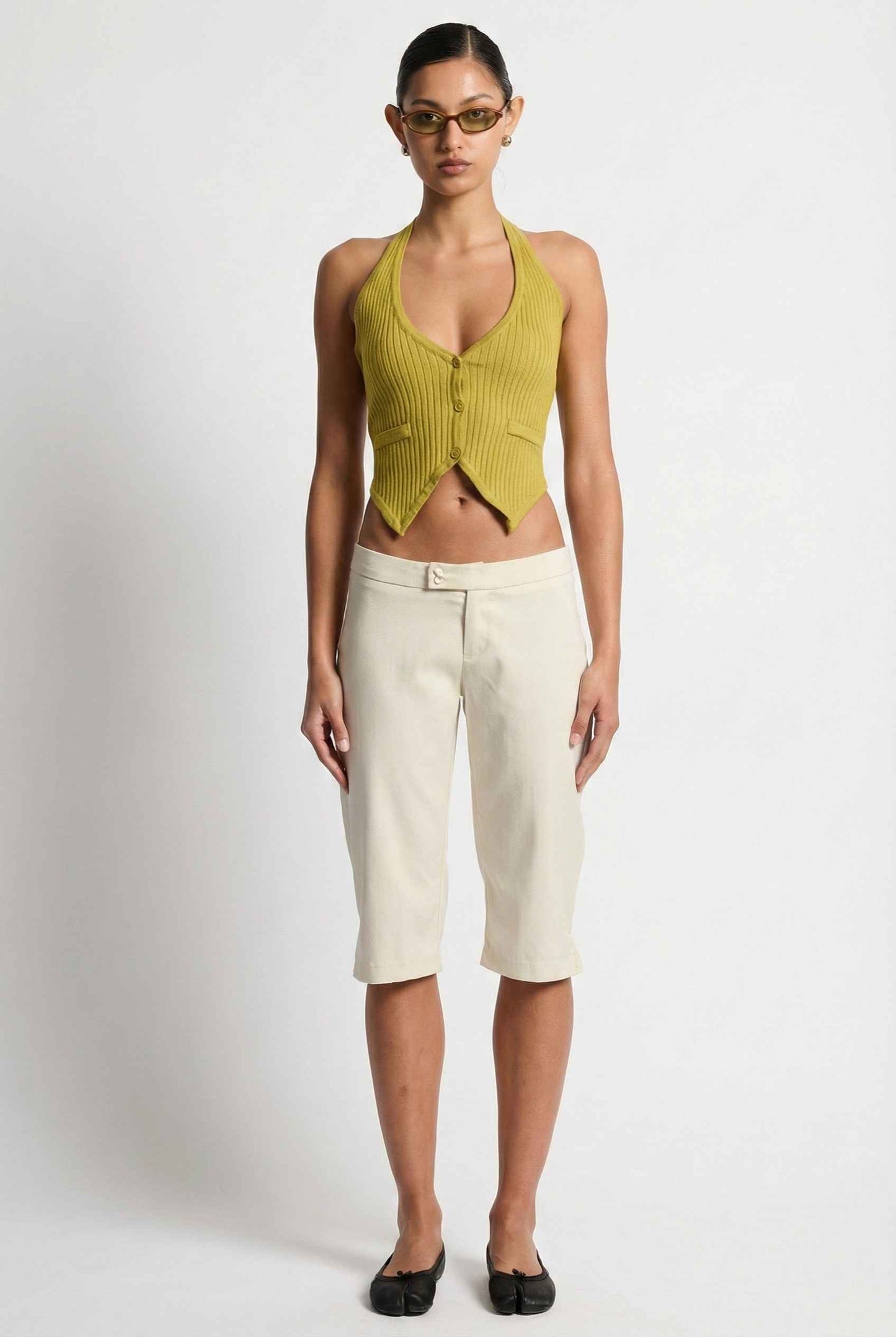 Model wearing Elise Shorts in Ivory Tailored Mid-Rise Bermuda Shorts with halter top and flats on plain background