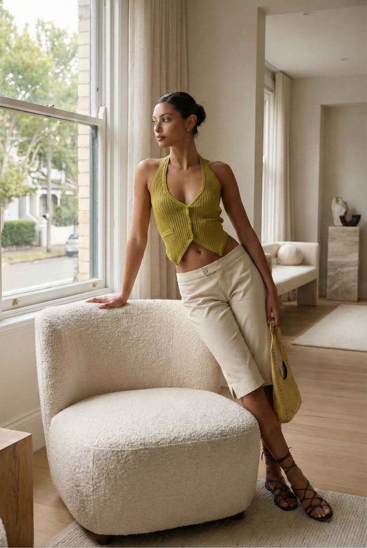 Model wearing Elise Shorts in Ivory Tailored Mid-Rise Bermuda Shorts with halter top and tie-up sandals posing in luxury living room