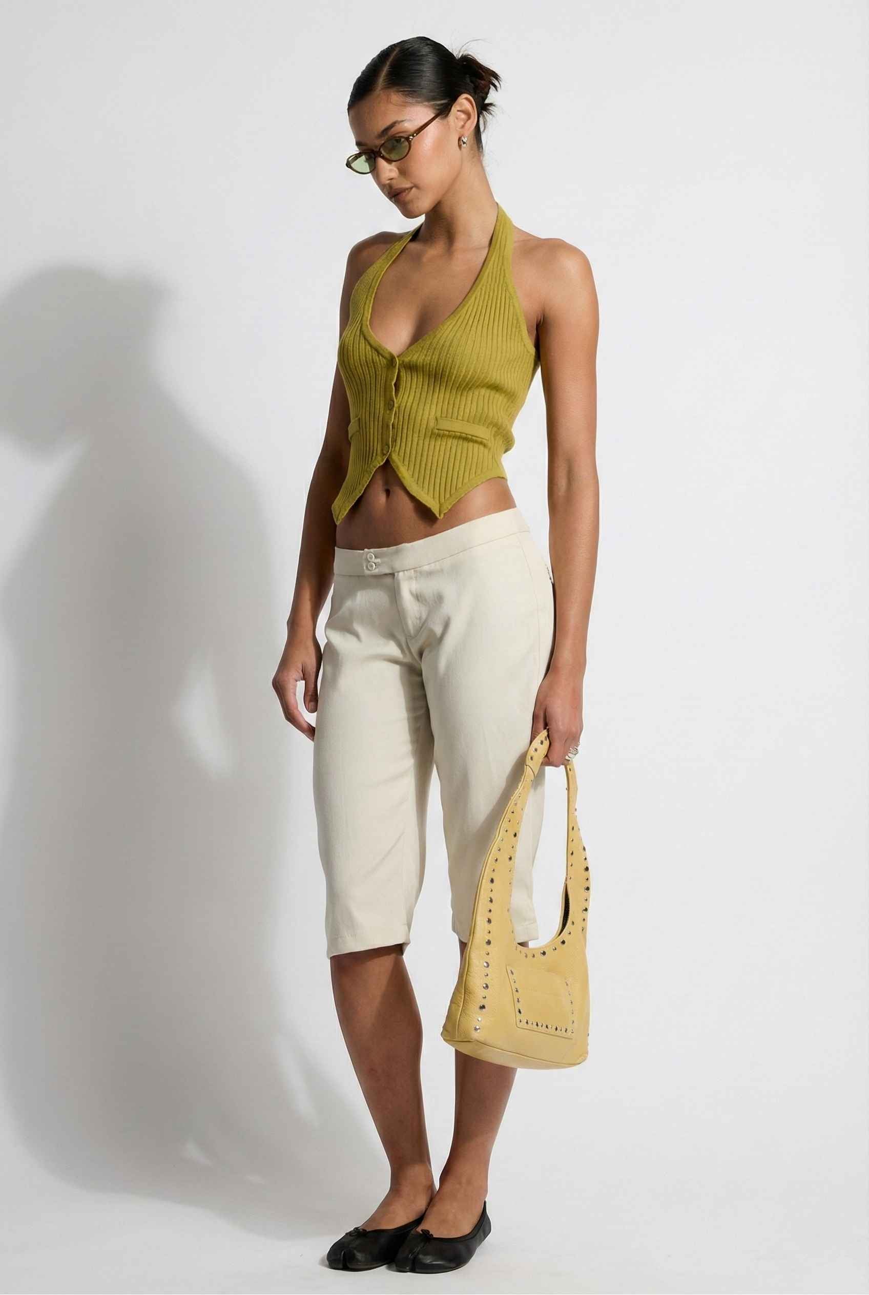 Model wearing Elise Shorts in Ivory Tailored Mid-Rise Bermuda Shorts with halter top and flats on plain background