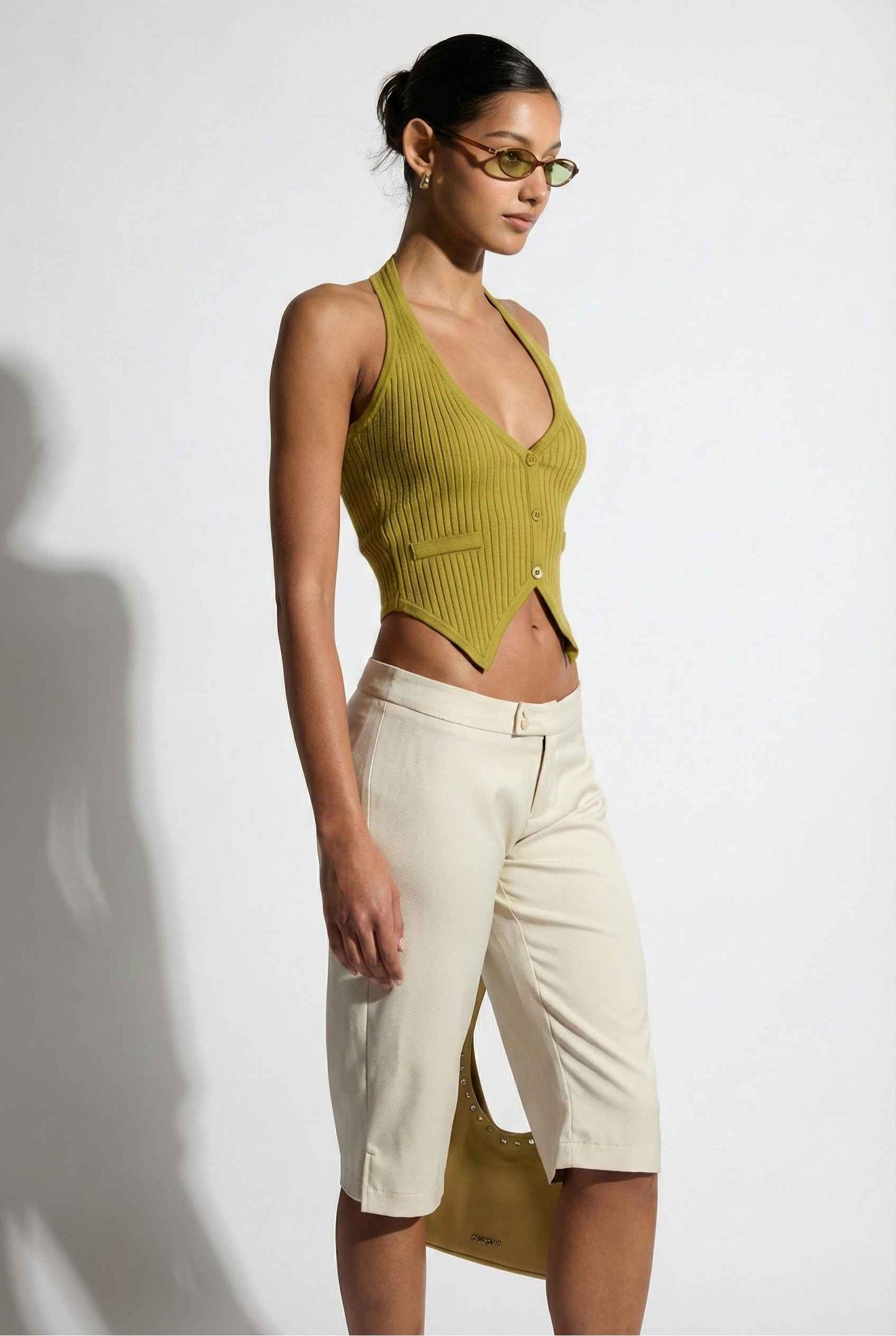 Model wearing Elise Shorts in Ivory Tailored Mid-Rise Bermuda Shorts with halter top and flats on plain background