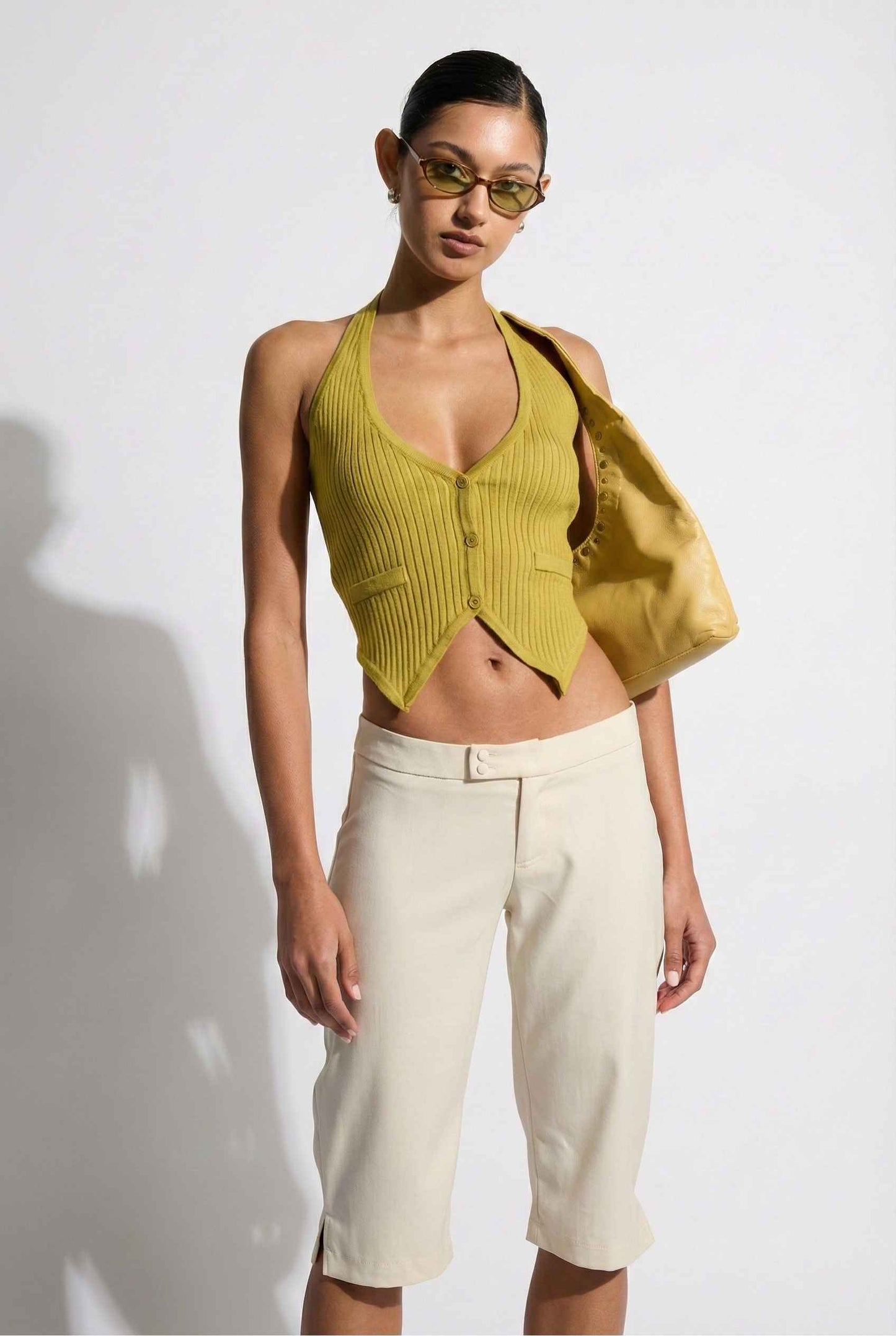 Model wearing Elise Shorts in Ivory Tailored Mid-Rise Bermuda Shorts with halter top and flats on plain background