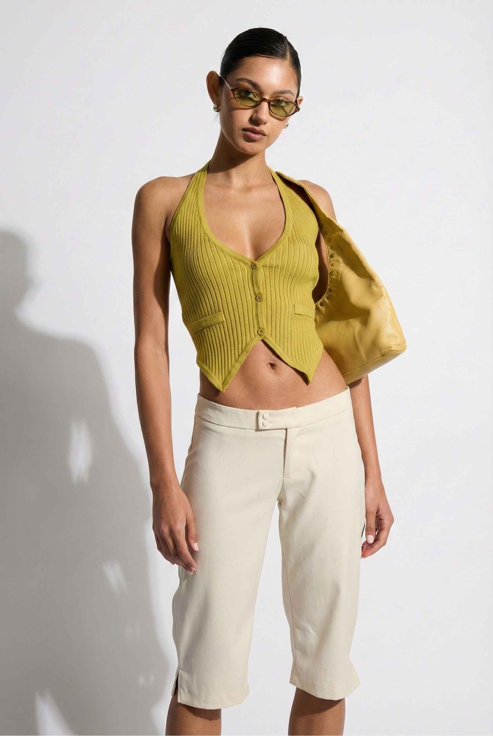 Model wearing Elise Shorts in Ivory Tailored Mid-Rise Bermuda Shorts with halter top and flats on plain background