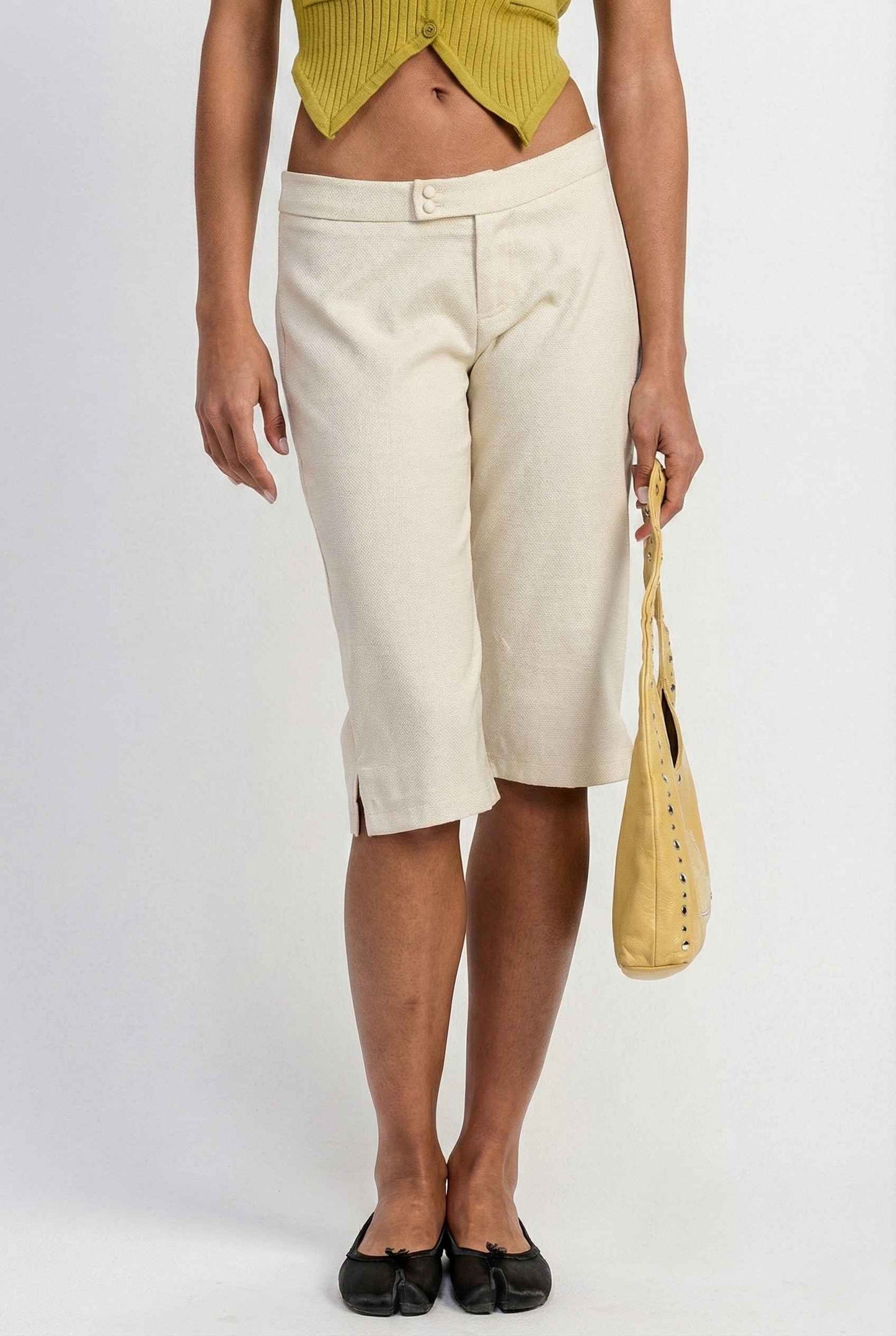 Model wearing Elise Shorts in Ivory Tailored Mid-Rise Bermuda Shorts with halter top and flats on plain background