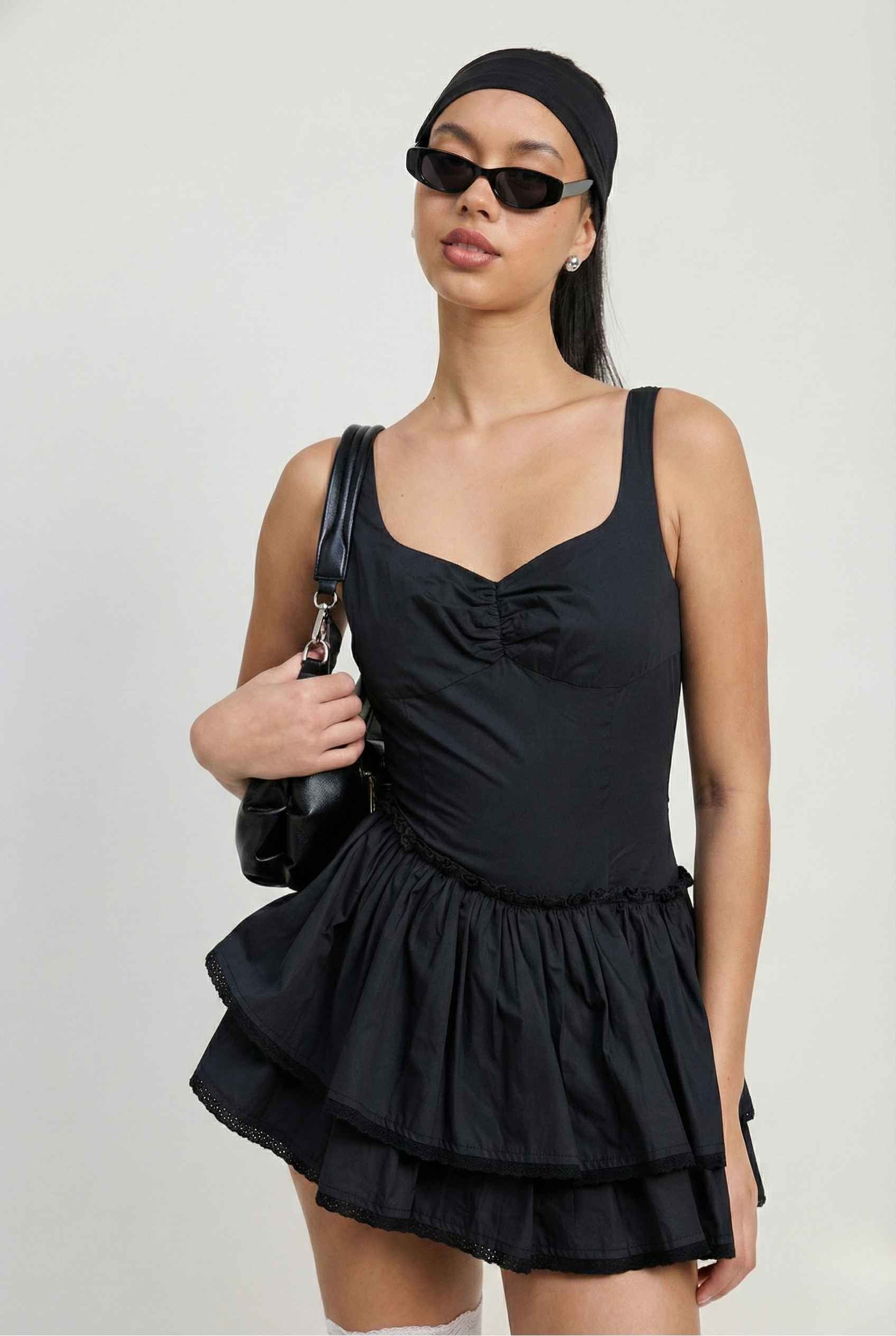 Woman wearing a Elodie Mini Black Tiered Ruffle Cotton Mini Dress with ruffled layers on a plain background