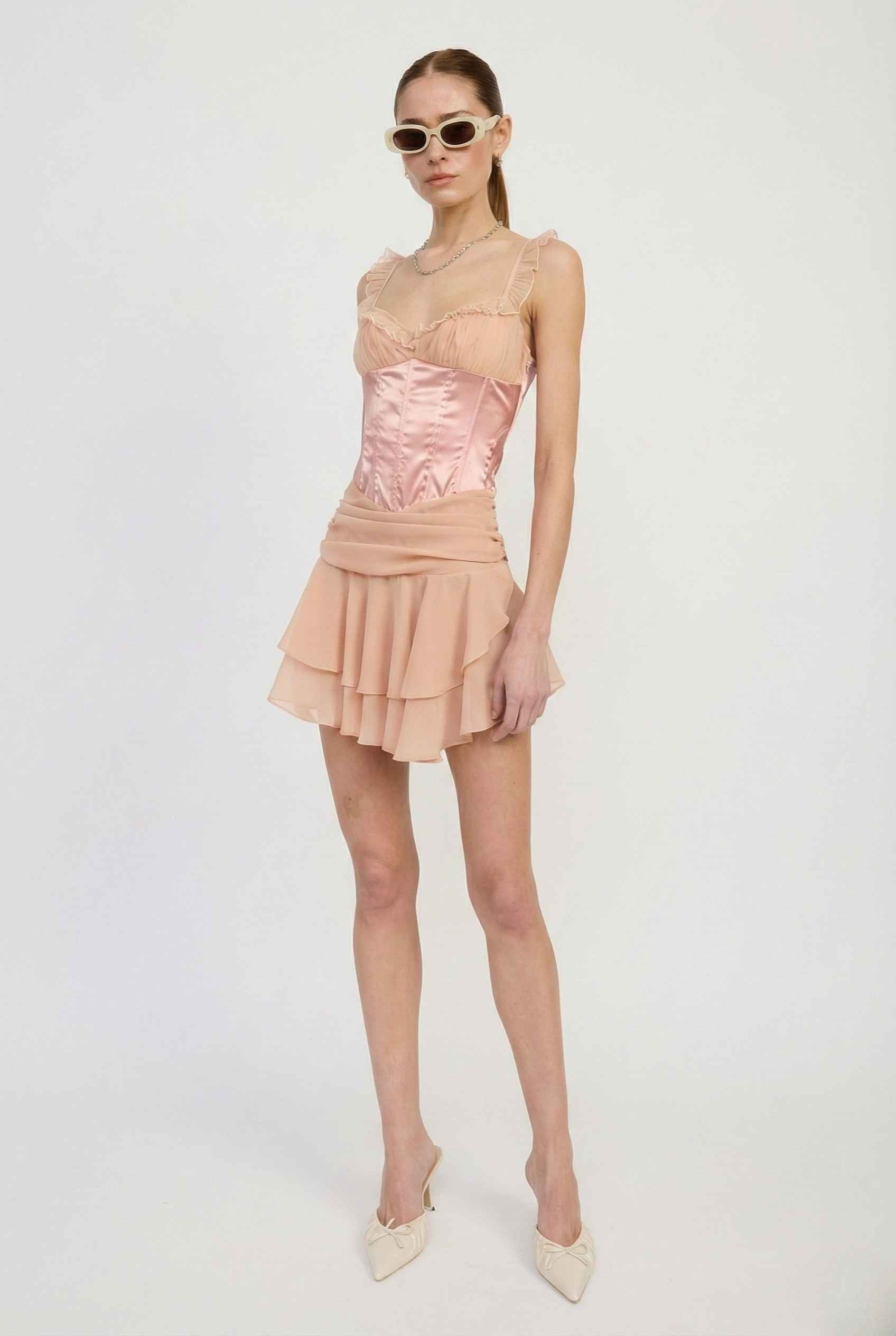 Woman wearing a Elodie Mini Pink Satin & Mesh Ruffle Bustier Dress with a white background