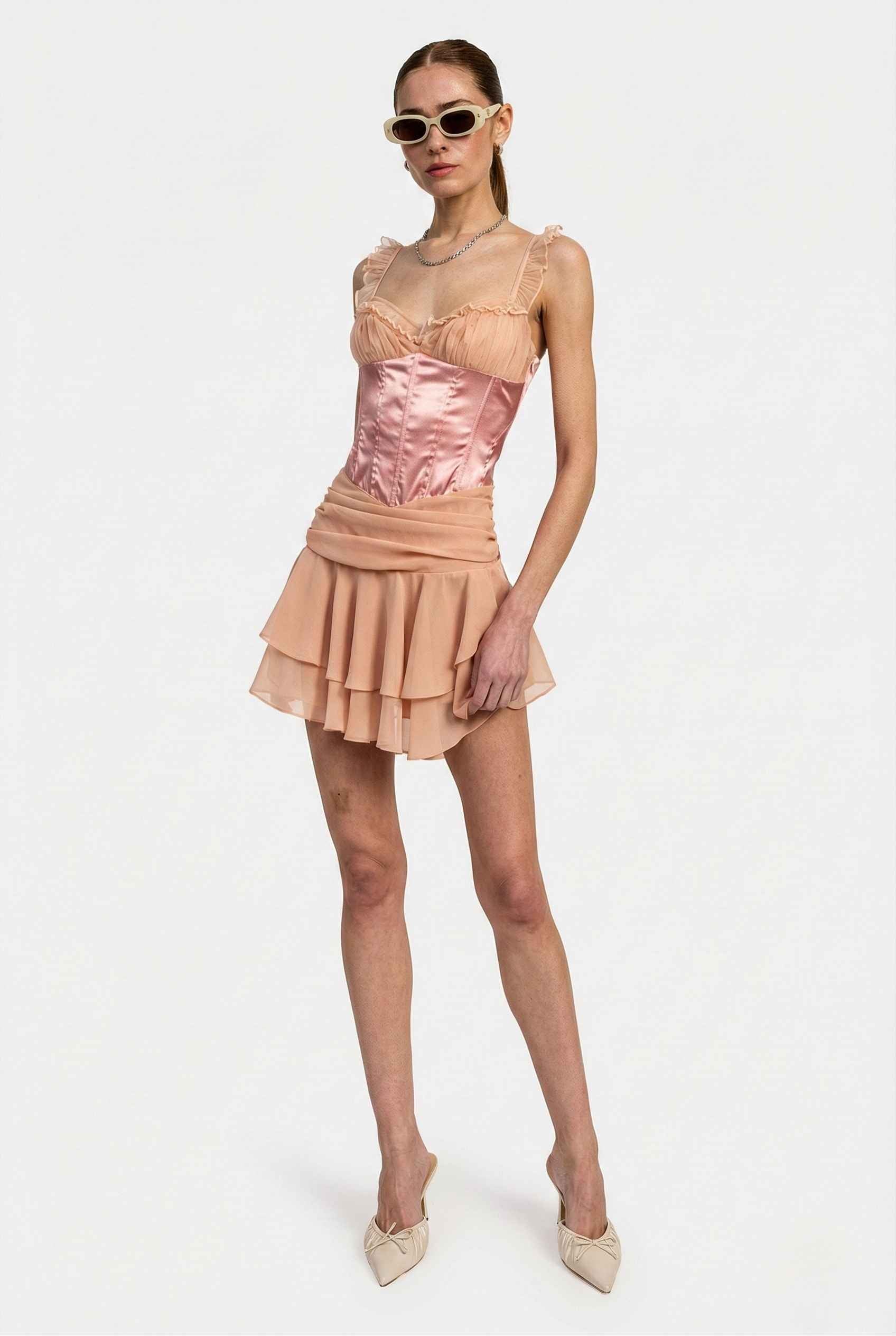 Woman wearing a Elodie Mini Pink Satin & Mesh Ruffle Bustier Dress with sunglasses on a white background