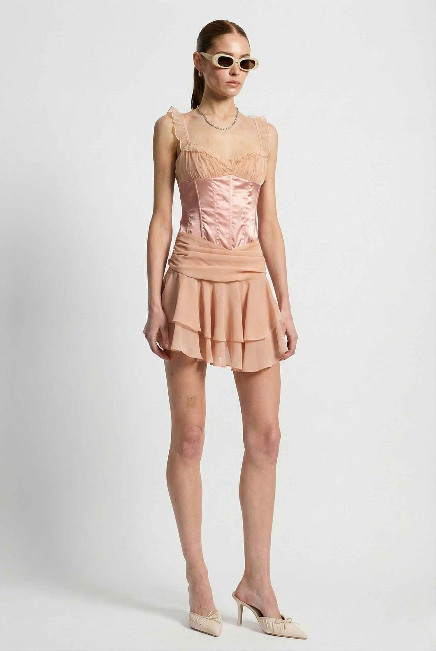 Woman wearing a Elodie Mini Pink Satin & Mesh Ruffle Bustier Dress with a white background
