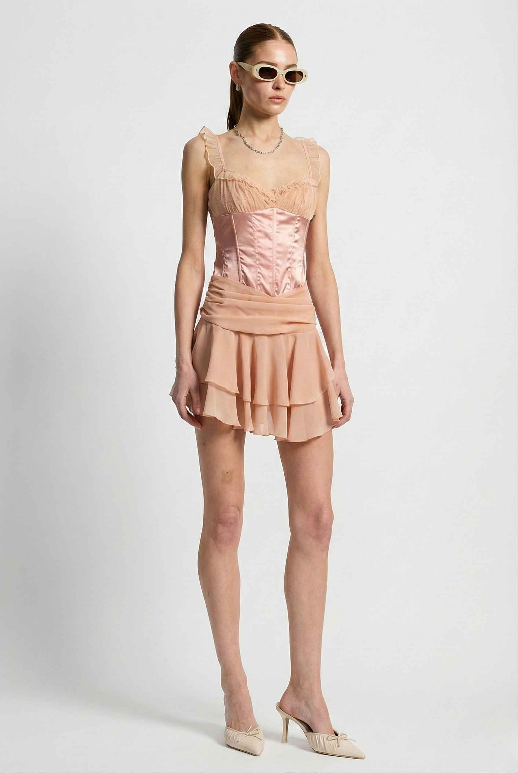 Woman wearing a Elodie Mini Pink Satin & Mesh Ruffle Bustier Dress with a white background
