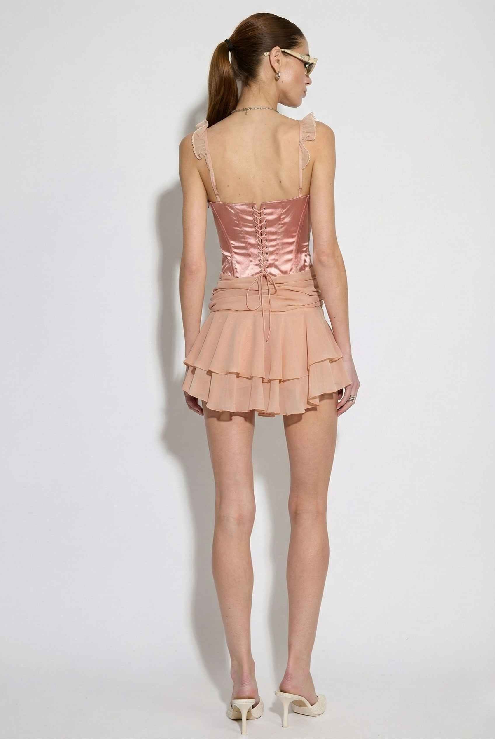 Woman wearing a Elodie Mini Pink Satin & Mesh Ruffle Bustier Dress against a white background