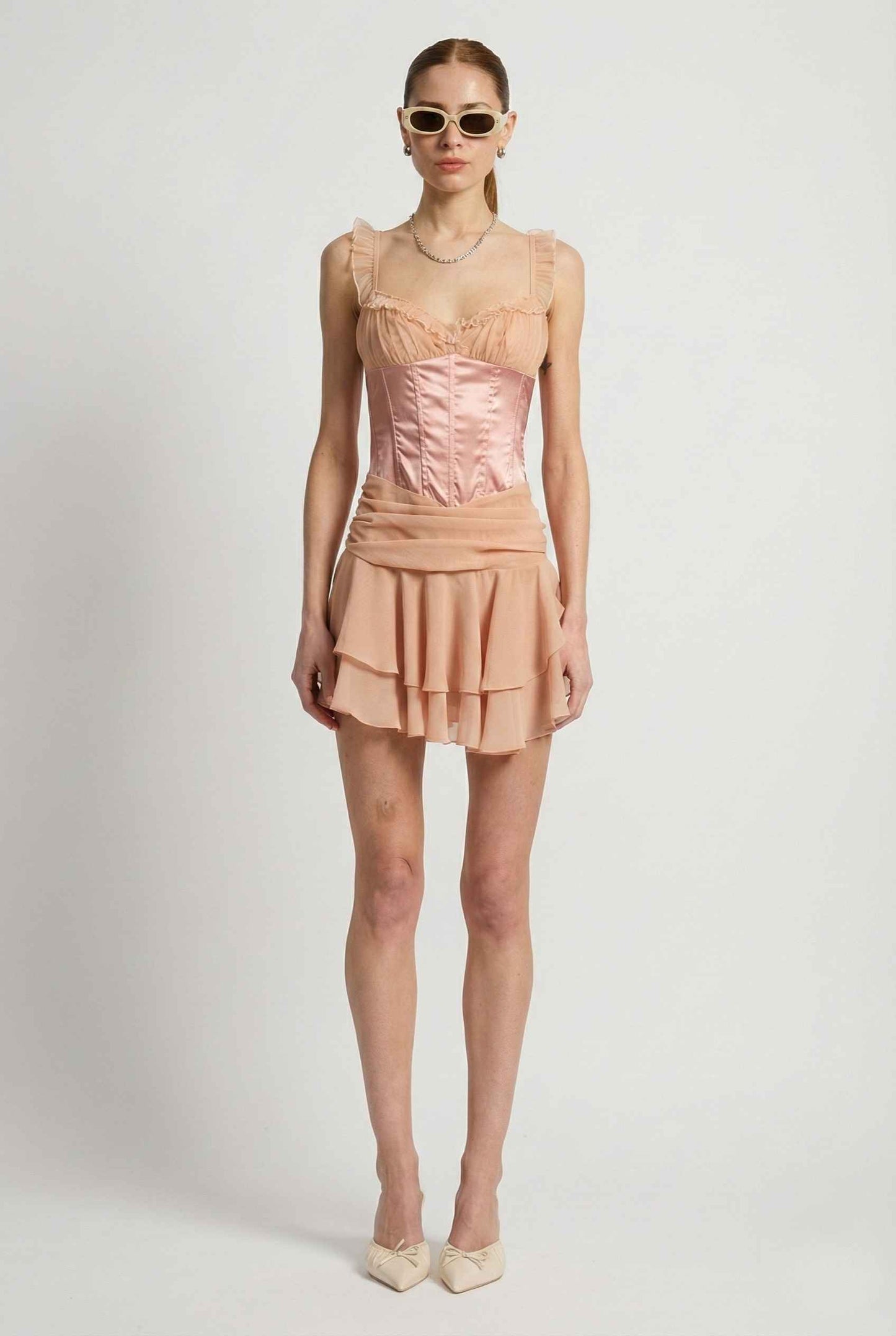 Woman wearing a Elodie Mini Pink Satin & Mesh Ruffle Bustier Dress with a white background