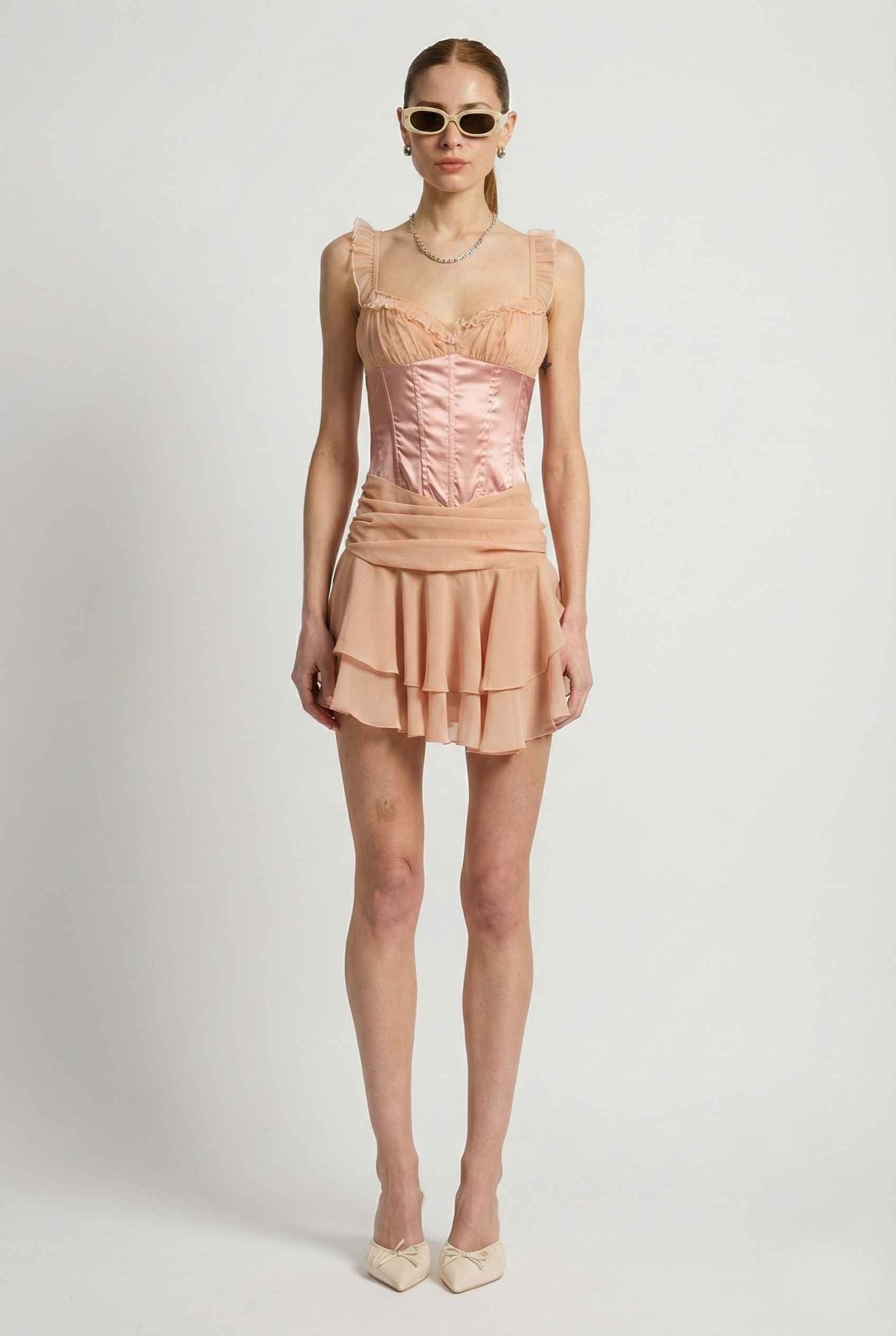 Woman wearing a Elodie Mini Pink Satin & Mesh Ruffle Bustier Dress with a white background