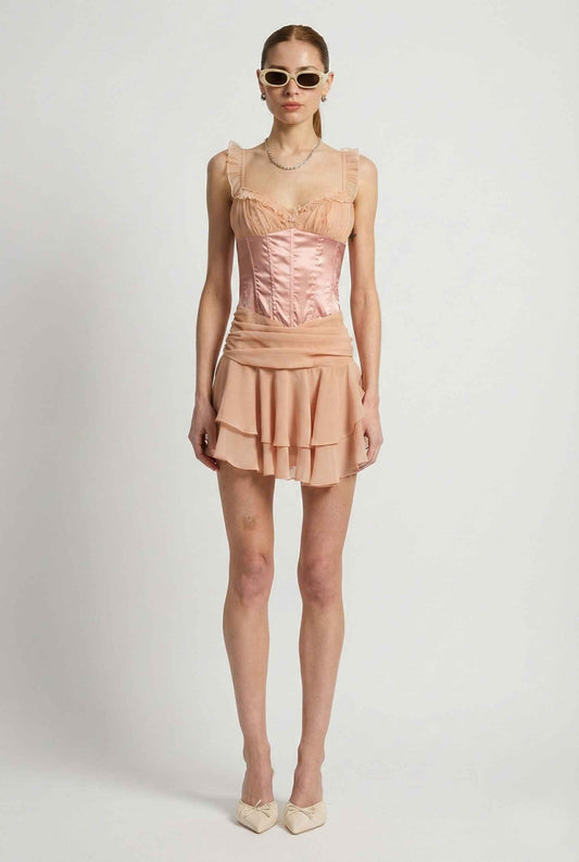 Woman wearing a Elodie Mini Pink Satin & Mesh Ruffle Bustier Dress with a white background
