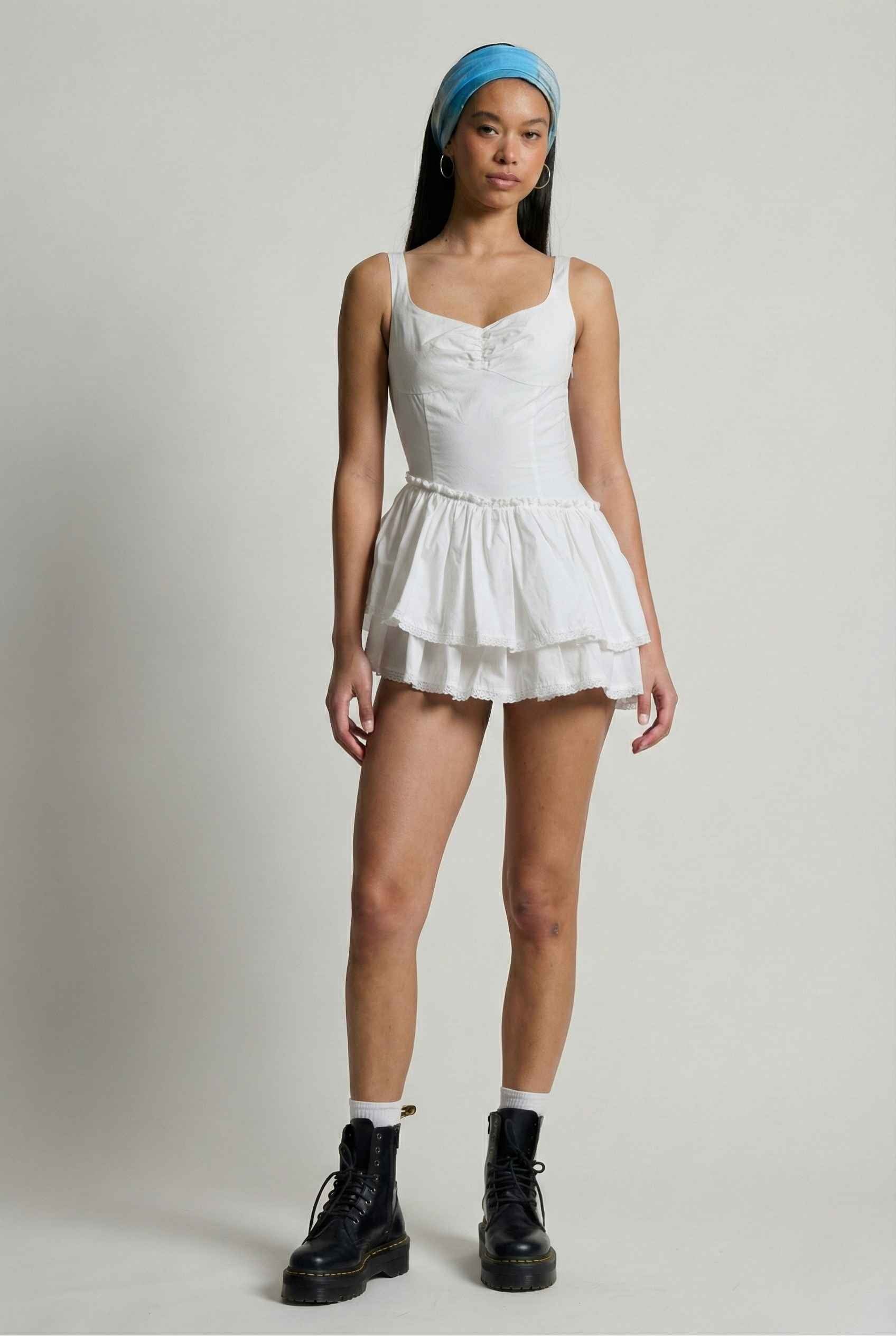 Person wearing a Elodie Mini White Tiered Ruffle Cotton Mini Dress with a blue headscarf on a plain background