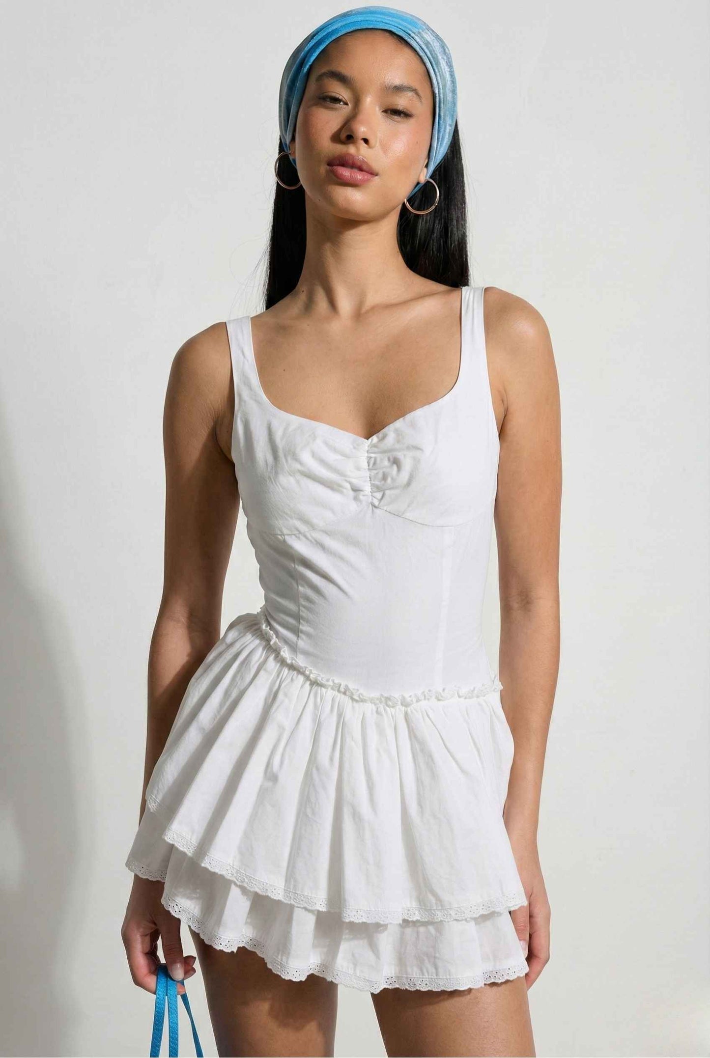 Woman wearing a Elodie Mini White Tiered Ruffle Cotton Mini Dress with a blue headscarf on a plain background