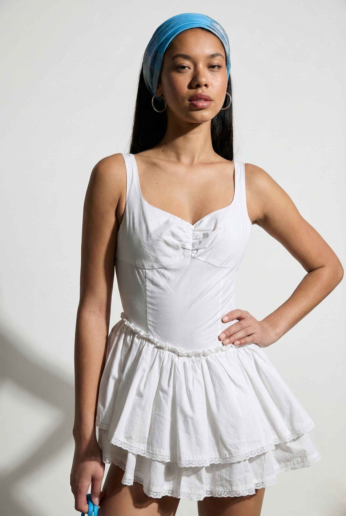 Woman wearing a Elodie Mini White Tiered Ruffle Cotton Mini Dress with a blue headscarf on a plain background