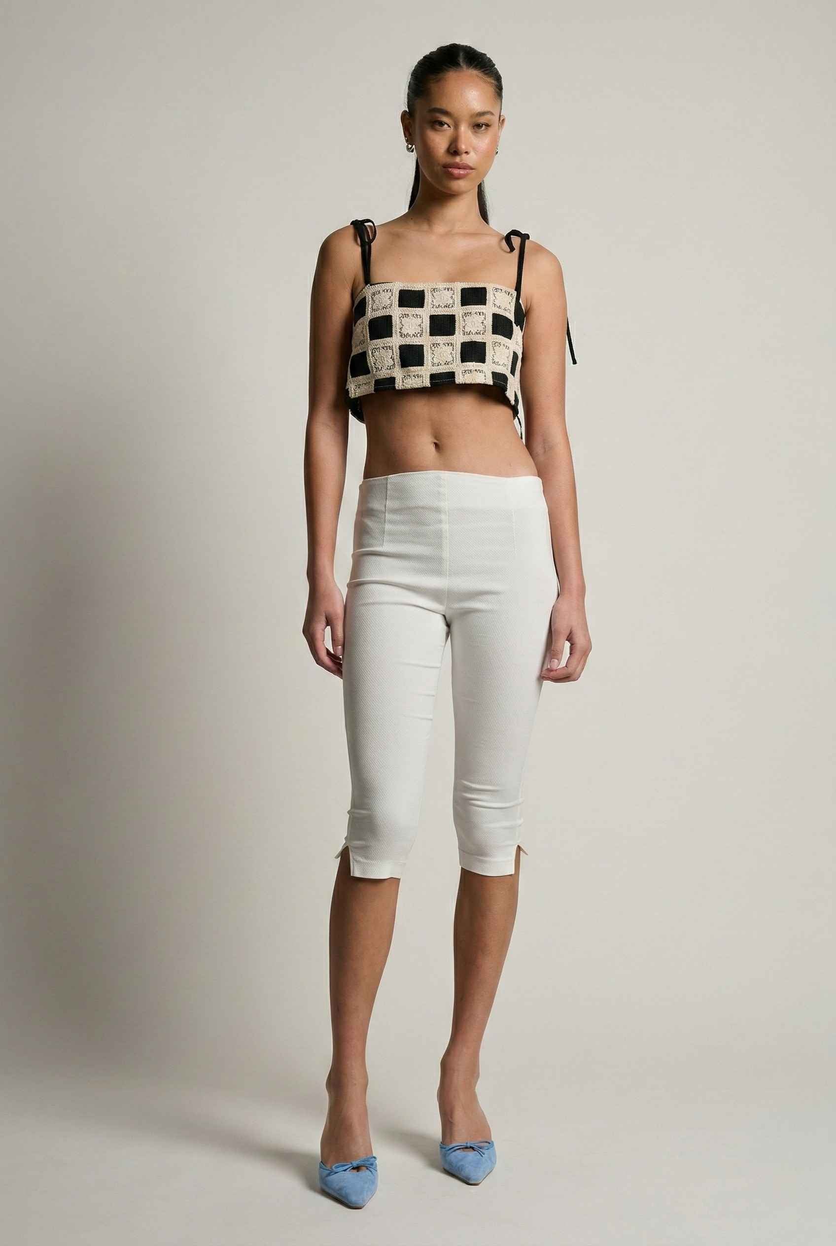 Model wearing Elodie Top in Black Jacquard Square Neck Cami with Ribbon Tie Straps with capri pants and heels on a plain background