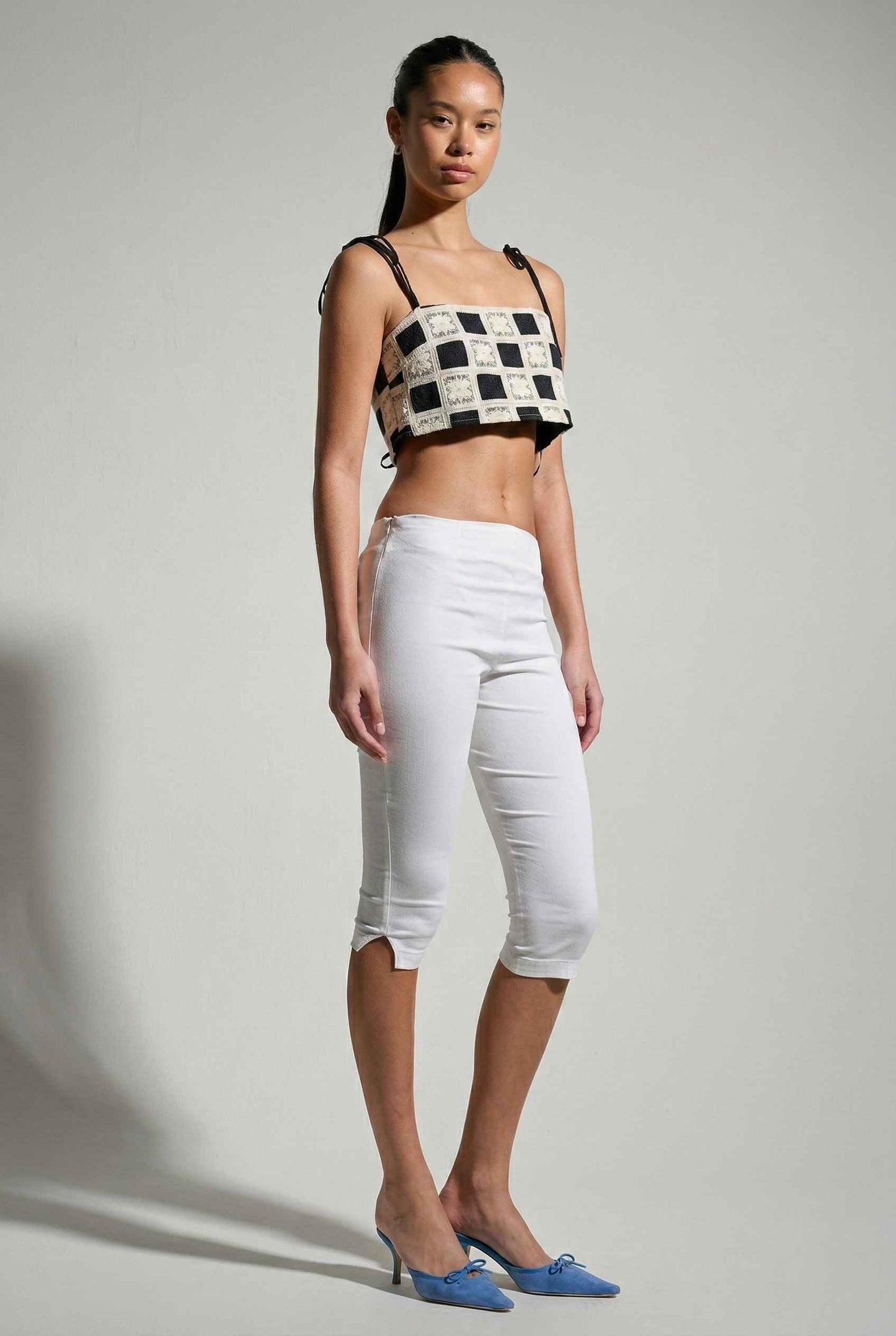 Model wearing Elodie Top in Black Jacquard Square Neck Cami with Ribbon Tie Straps with capri pants and heels on a plain background